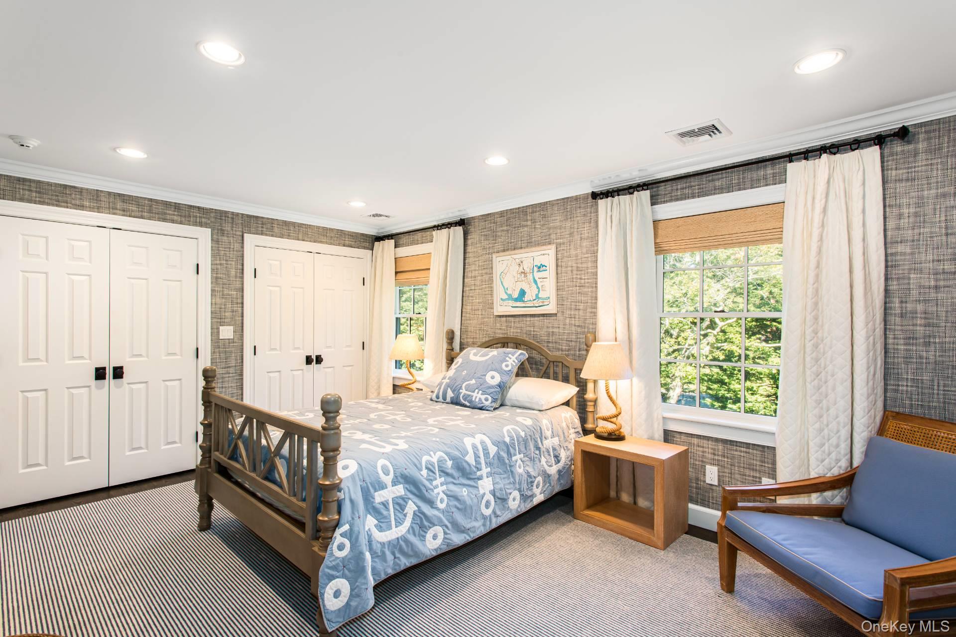 Bedroom with blue anchor-patterned bedding, gray textured walls, and bright windows.