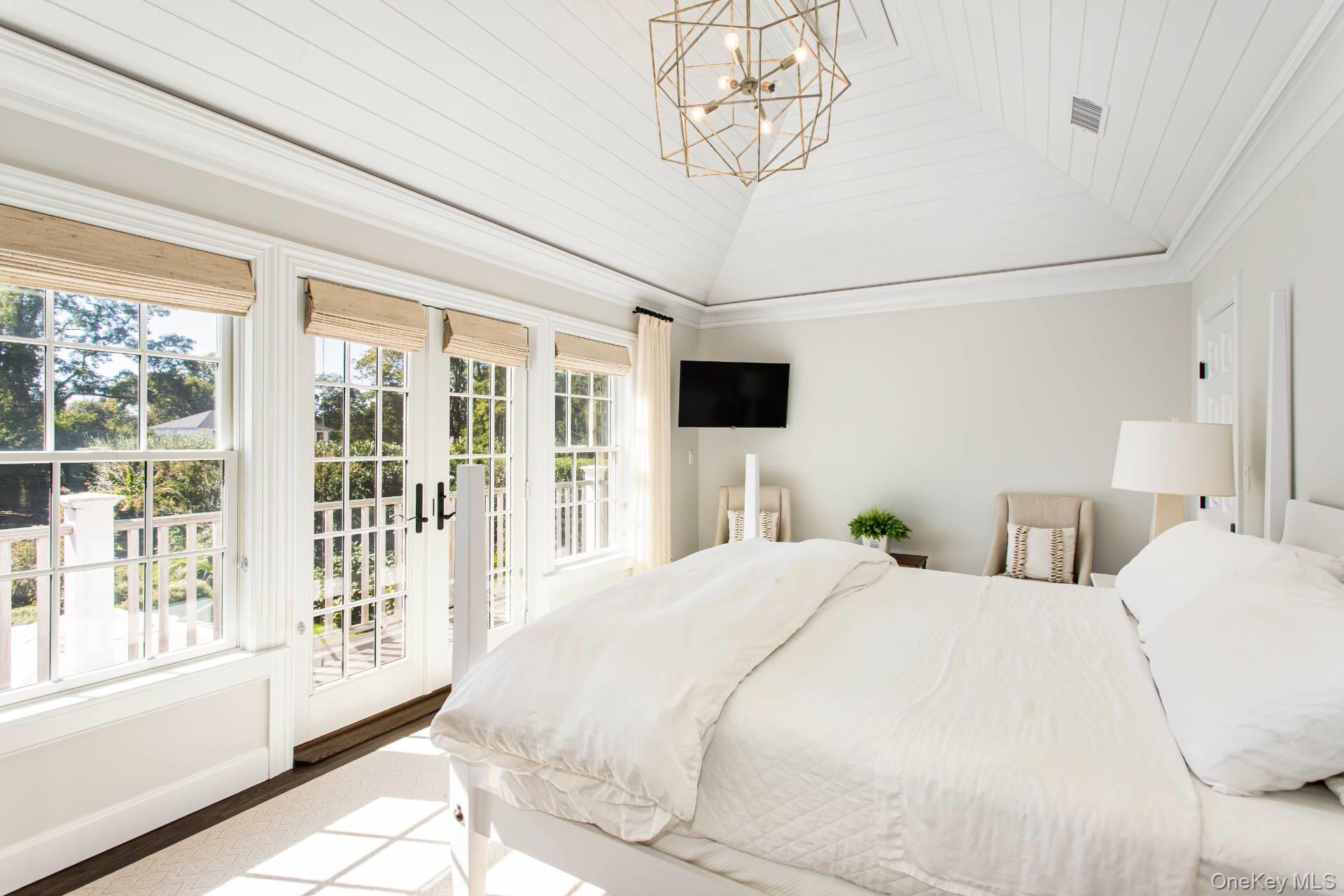 Bright bedroom with a vaulted ceiling, tall windows, glass doors, and a white bed.