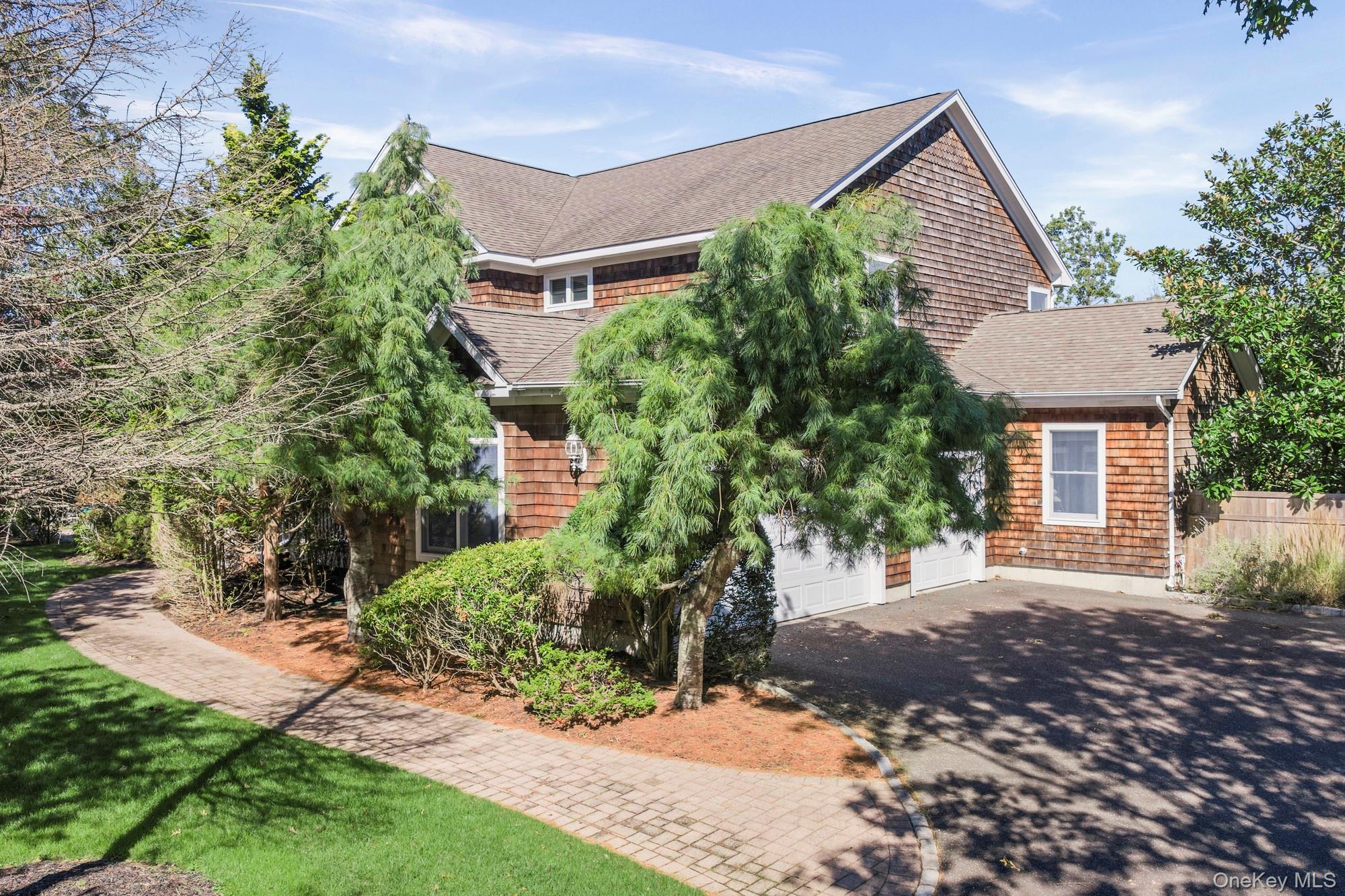 Two-story shingle-sided home with an attached garage, partly screened by mature trees and landscaping.