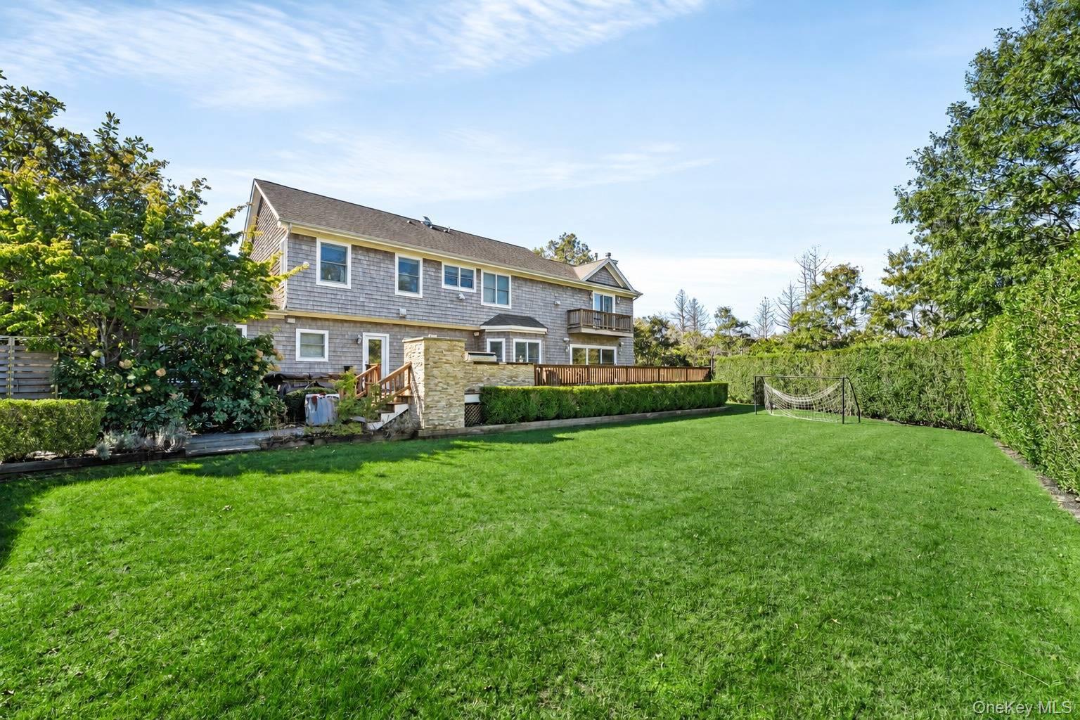 Rear of a shingle-sided house with a broad lawn, deck, hedges, and a soccer goal.