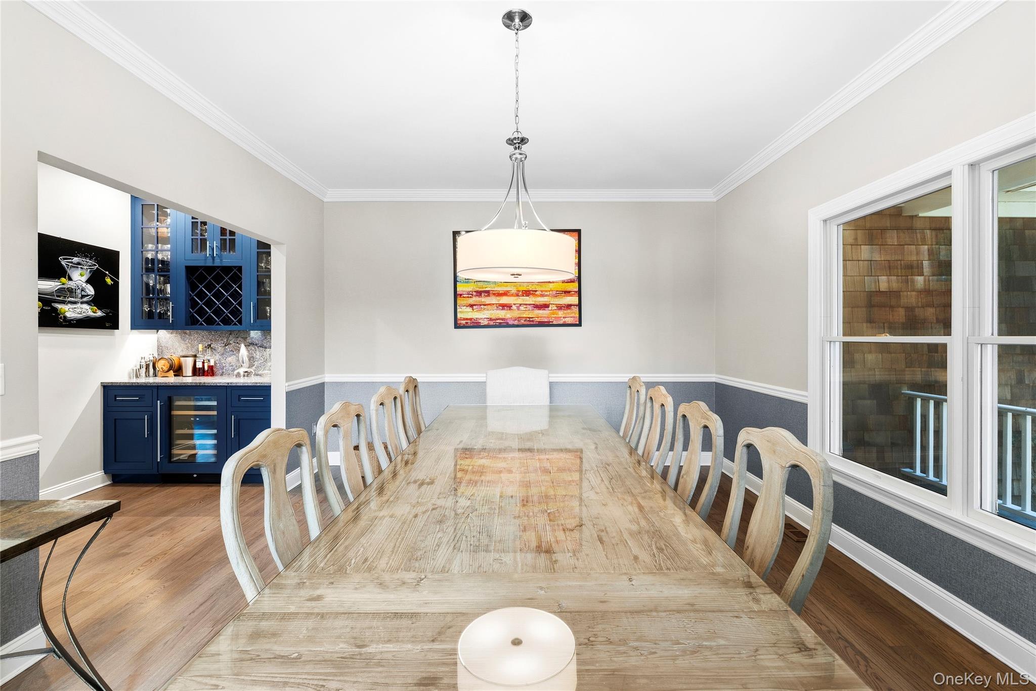 Dining room with a long rustic wood table, pale chairs, and blue built-in bar cabinetry.
