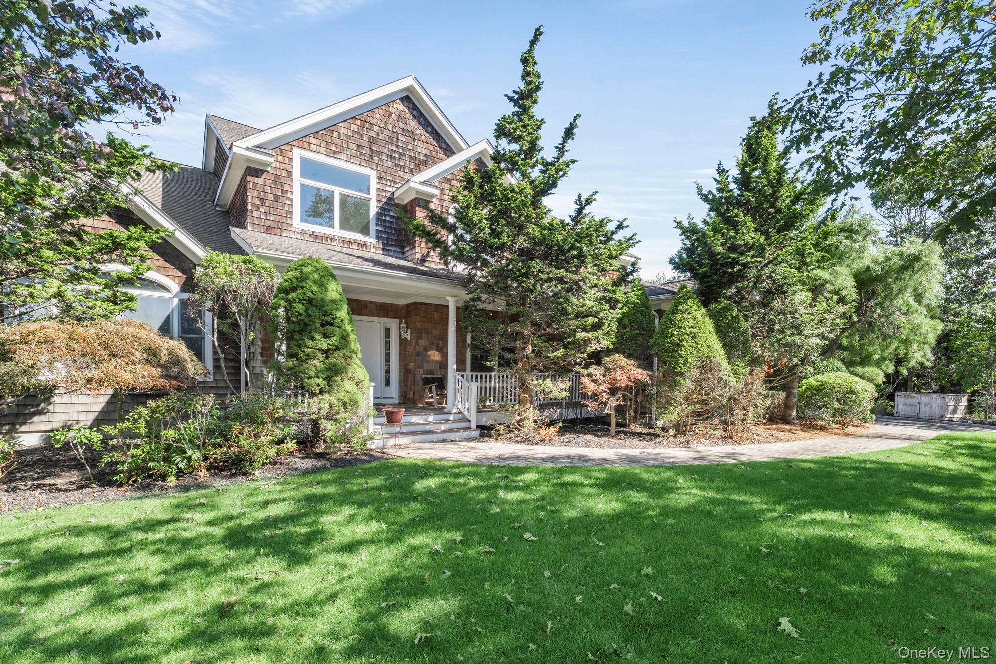 Shingle-sided home with a covered porch, mature trees, and a broad green lawn.