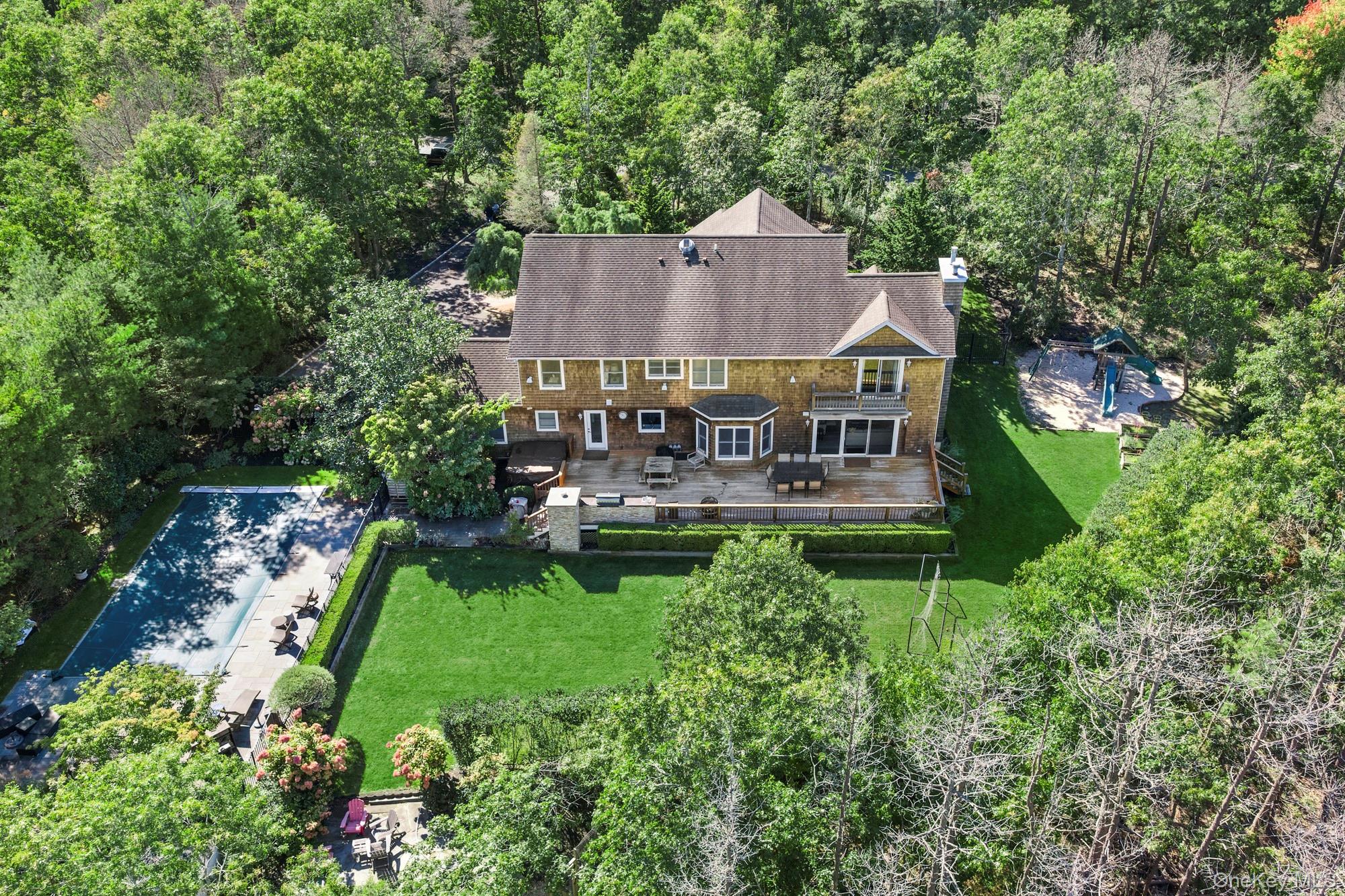 Aerial view of a shingle-sided home with a pool, spacious lawn, rear deck, and playset.