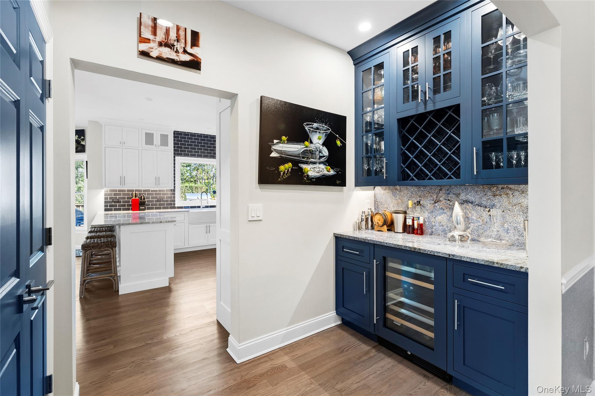 Wet bar with navy-blue cabinets, glass-front storage, and a built-in wine refrigerator beside the kitchen.