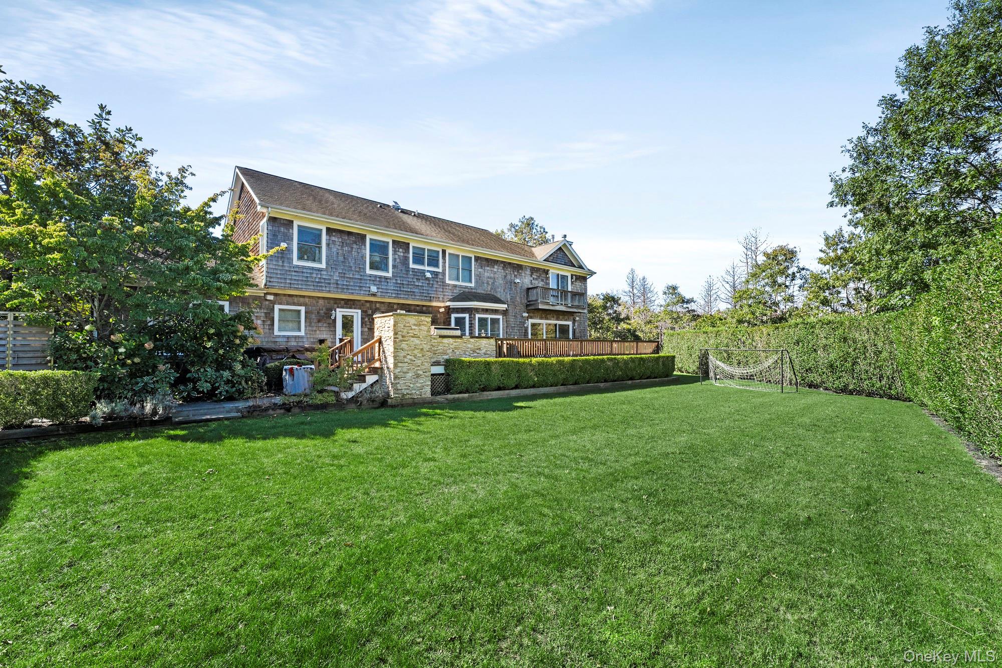 House rear and broad lawn with trimmed hedges, wooden deck, and soccer goal.