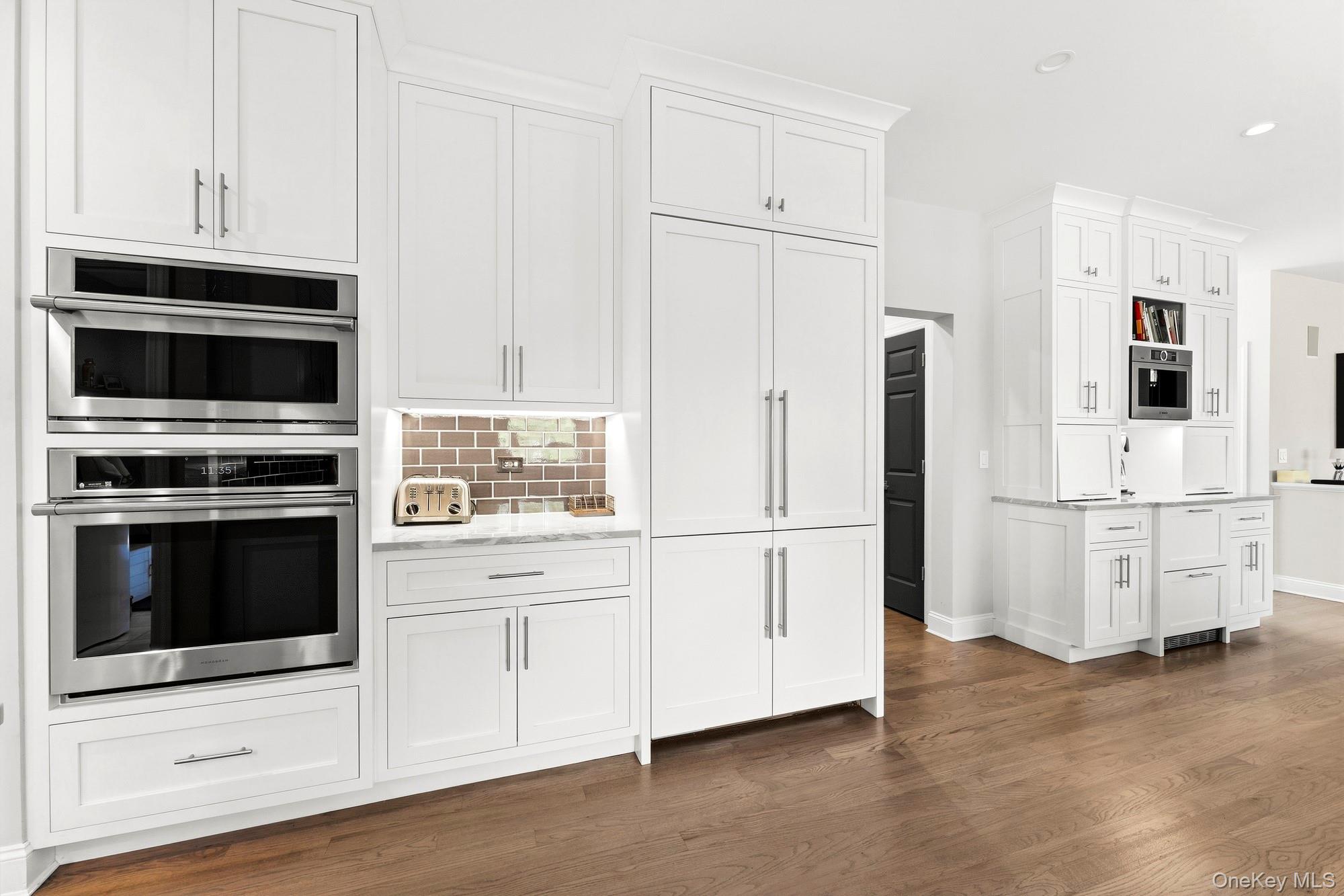 Bright white kitchen with double ovens, extensive cabinetry, and warm wood floors.
