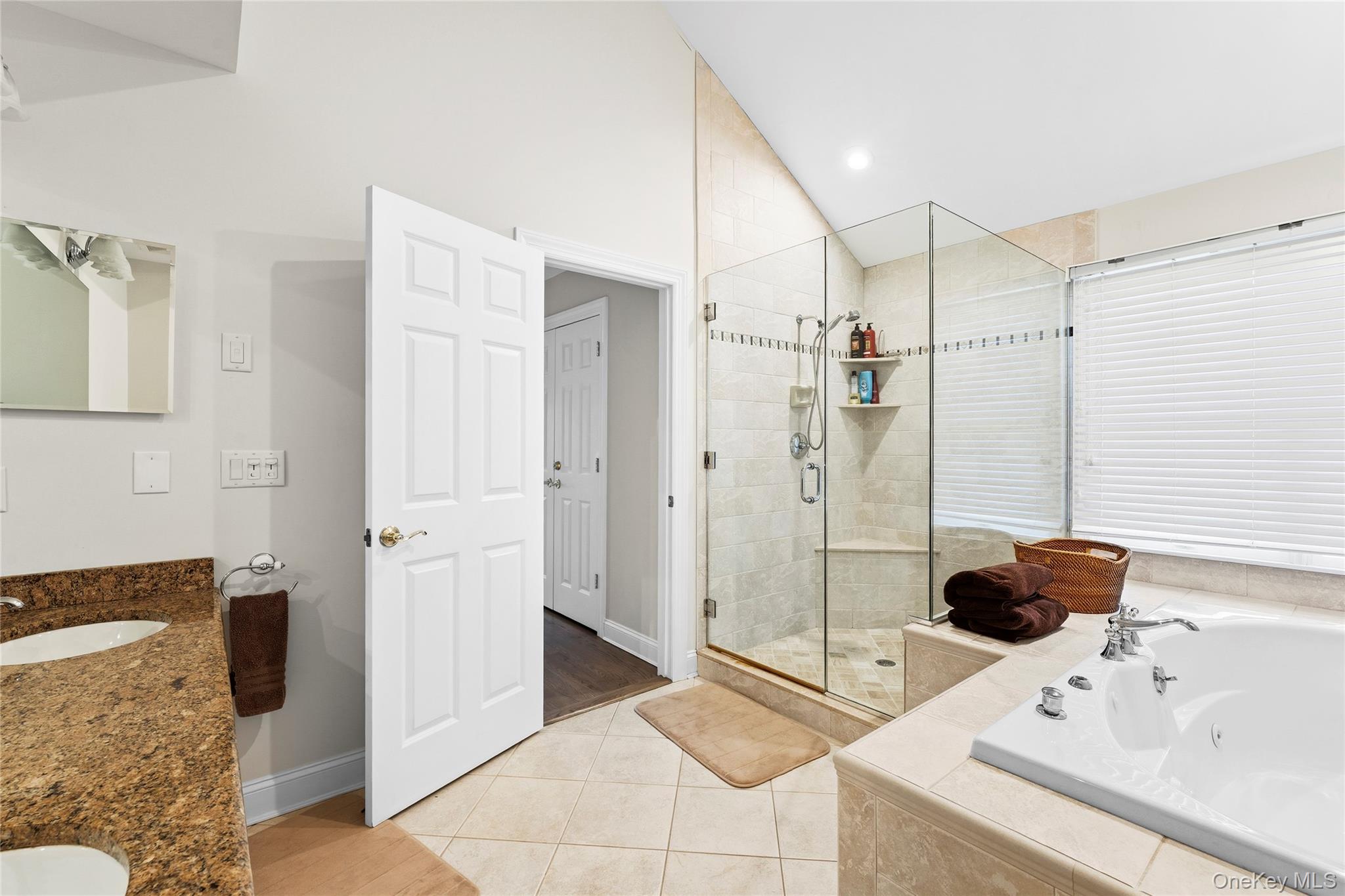 Bathroom with a large soaking tub, glass-enclosed shower, and granite double vanity.