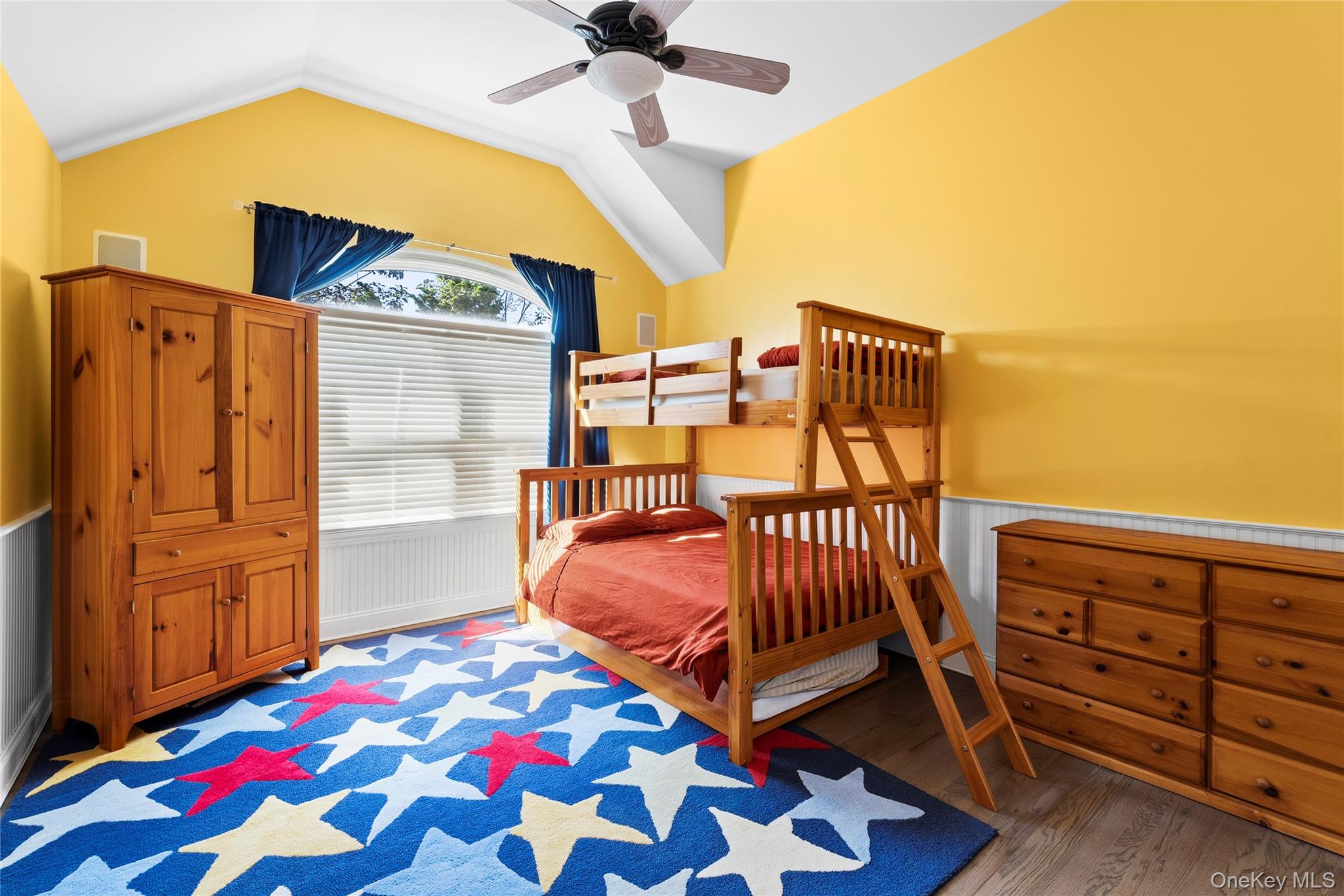 Bedroom with a wooden bunk bed, yellow walls, and a bold star-patterned rug.
