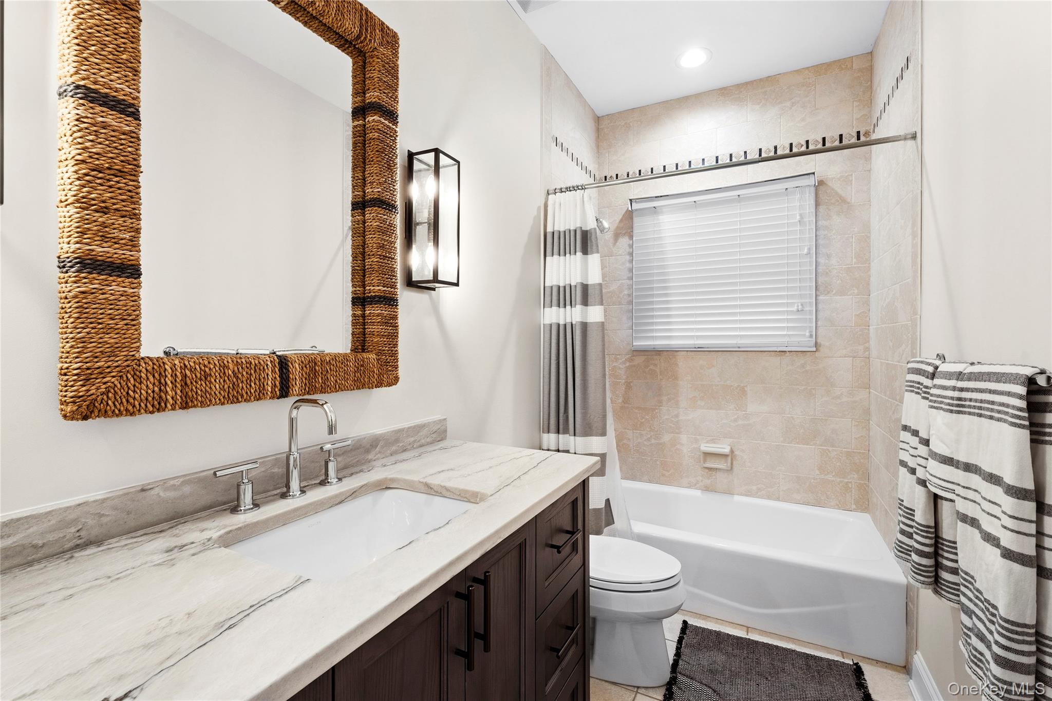 Bathroom with a marble vanity, rope-framed mirror, and tiled tub and shower.