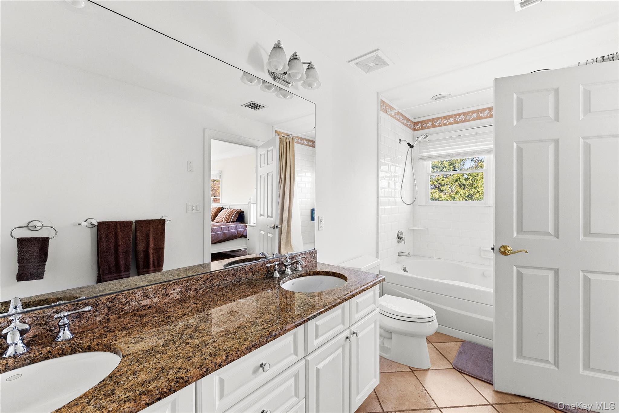 Bathroom with a granite double-sink vanity and a white-tiled tub and shower.
