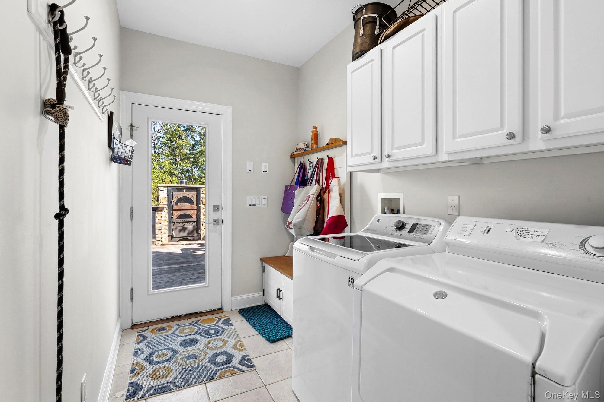 Laundry room with white washer and dryer, overhead cabinets, and a glass-panel door to the deck.