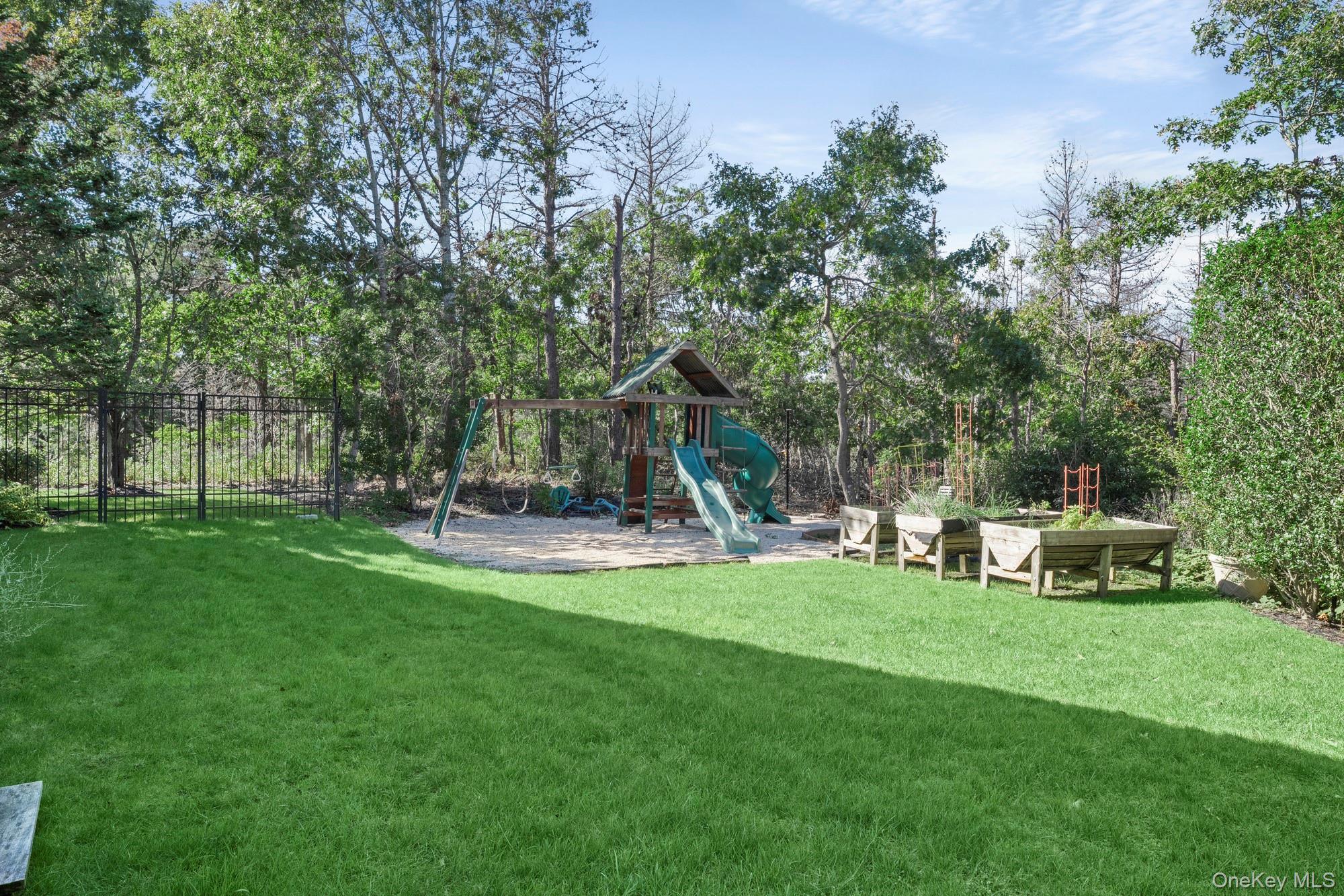 Backyard with a large playset, raised garden beds, and mature trees.