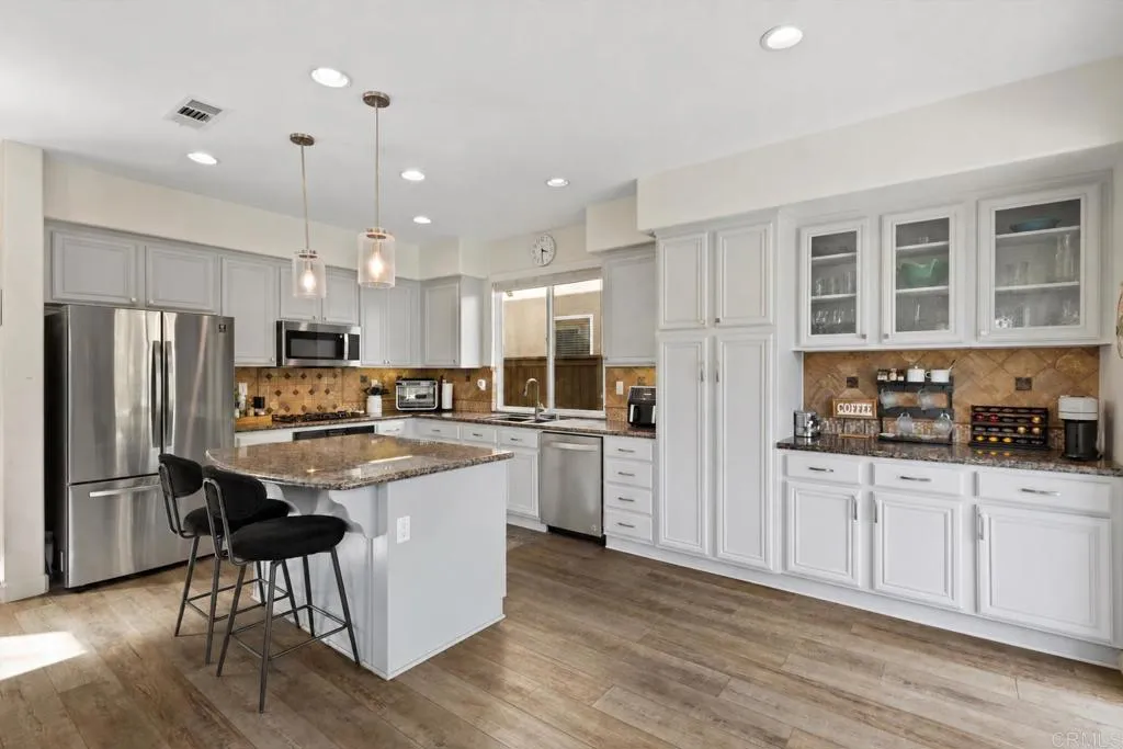 Kitchen with white cabinets, stainless steel appliances, and a granite island with two black stools.