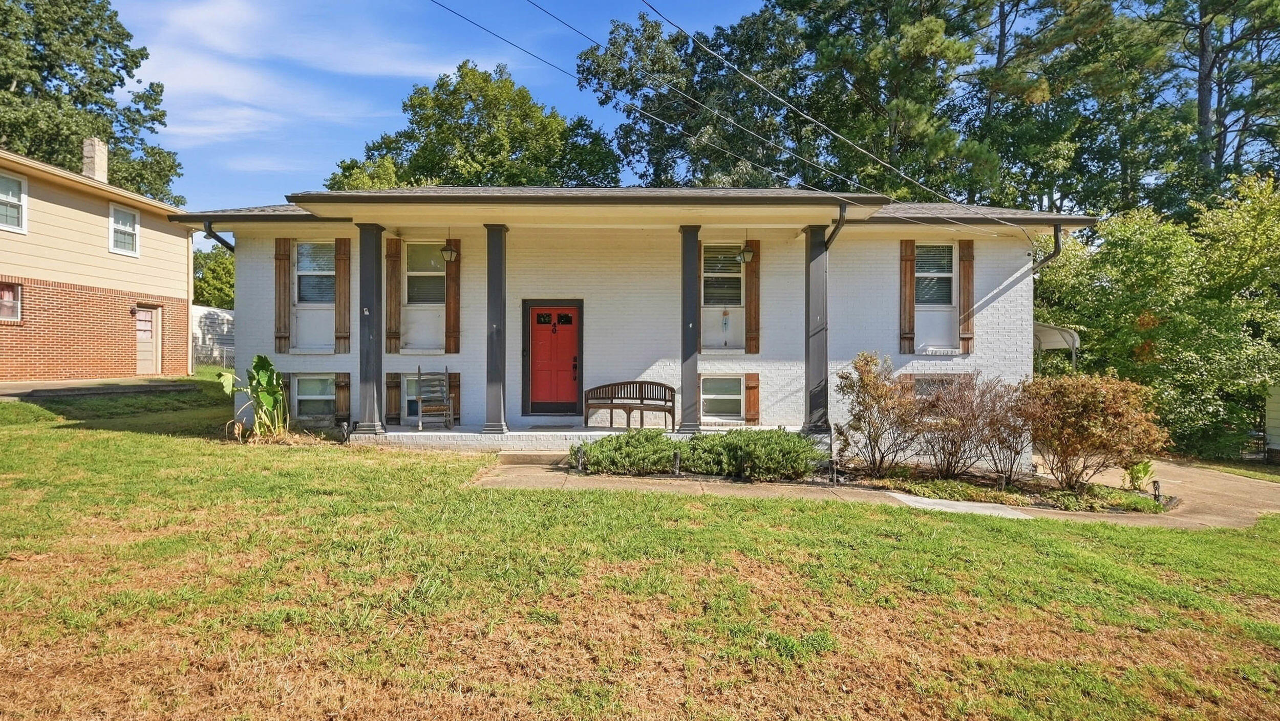 White-brick split-level house with a red front door, covered porch, and front lawn.