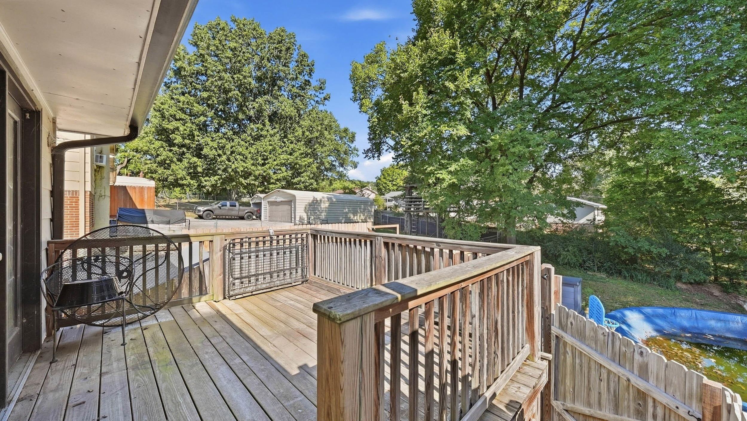 Wooden backyard deck with black metal chairs overlooking a fenced yard and blue above-ground pool.