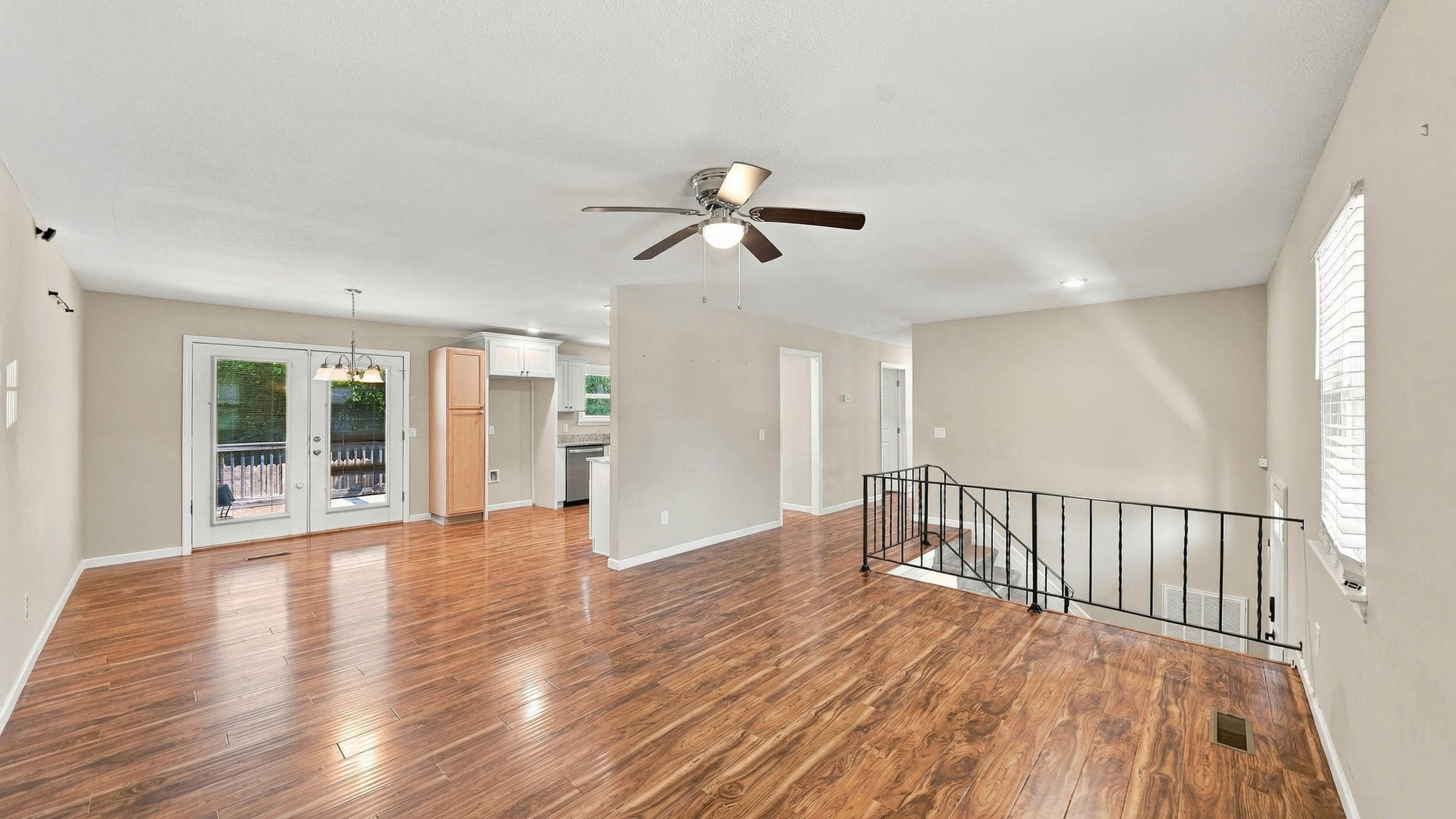 Open living and dining area with glossy wood-look floors, glass-panel doors, and a railing around the stair opening.