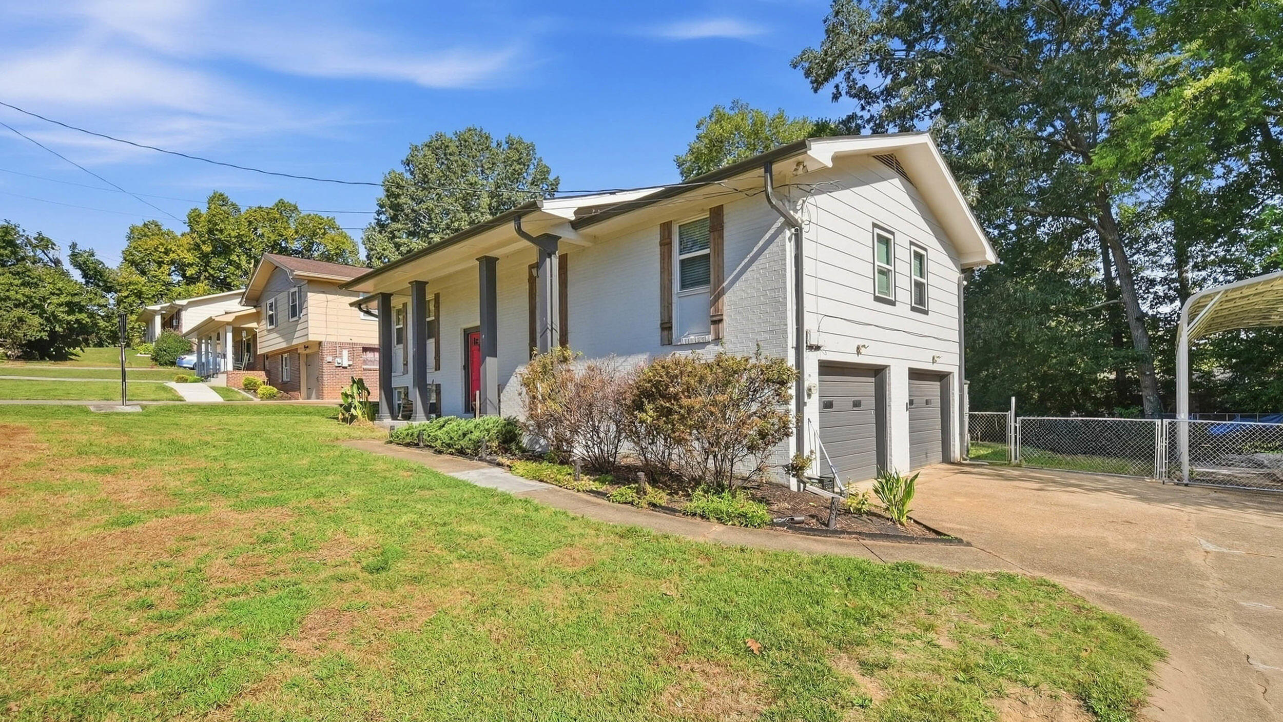 White split-level home with a red front door, two garage doors, and a broad driveway.