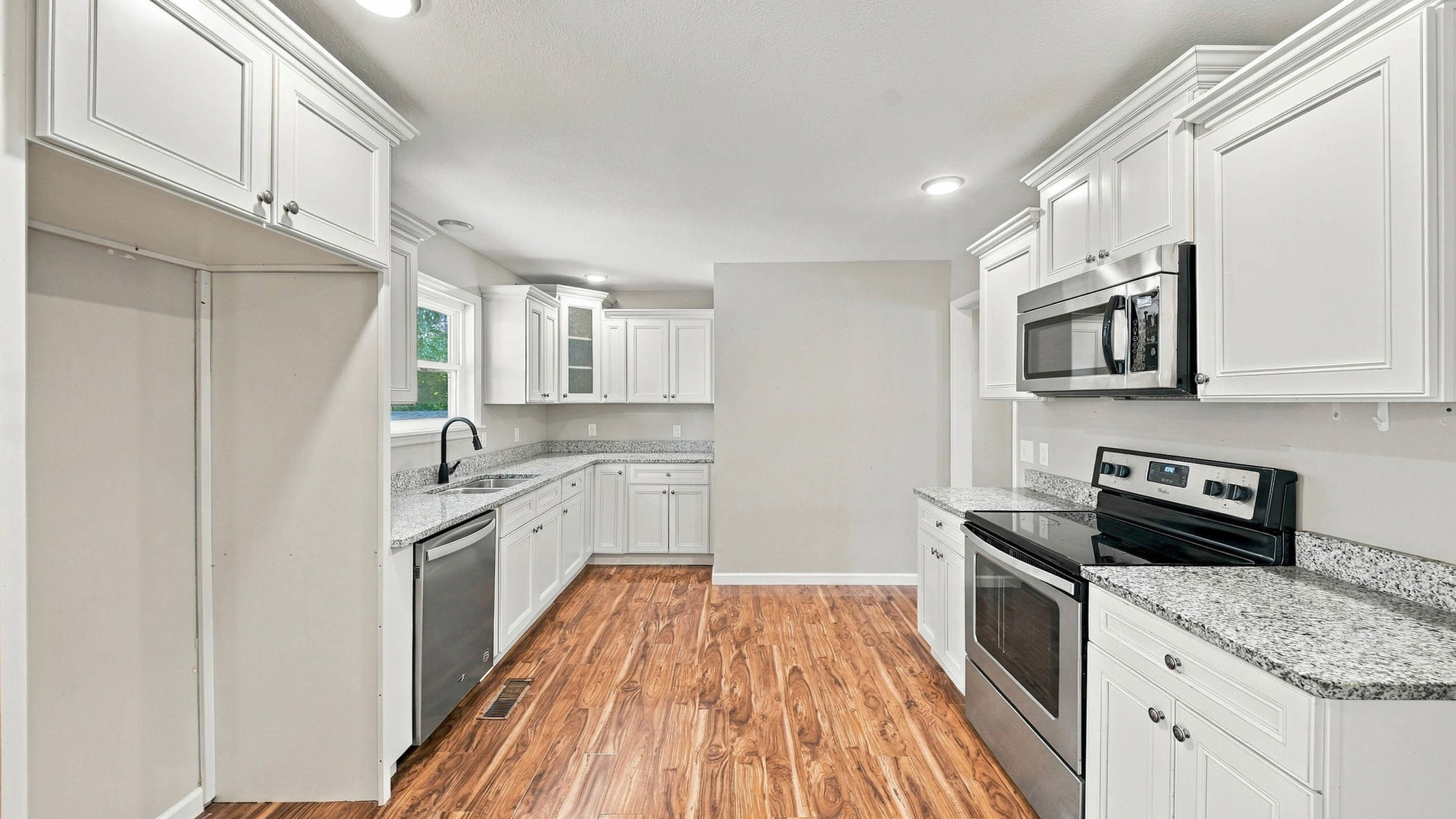 Kitchen with white cabinets, granite counters, stainless steel appliances, and wood-look flooring.