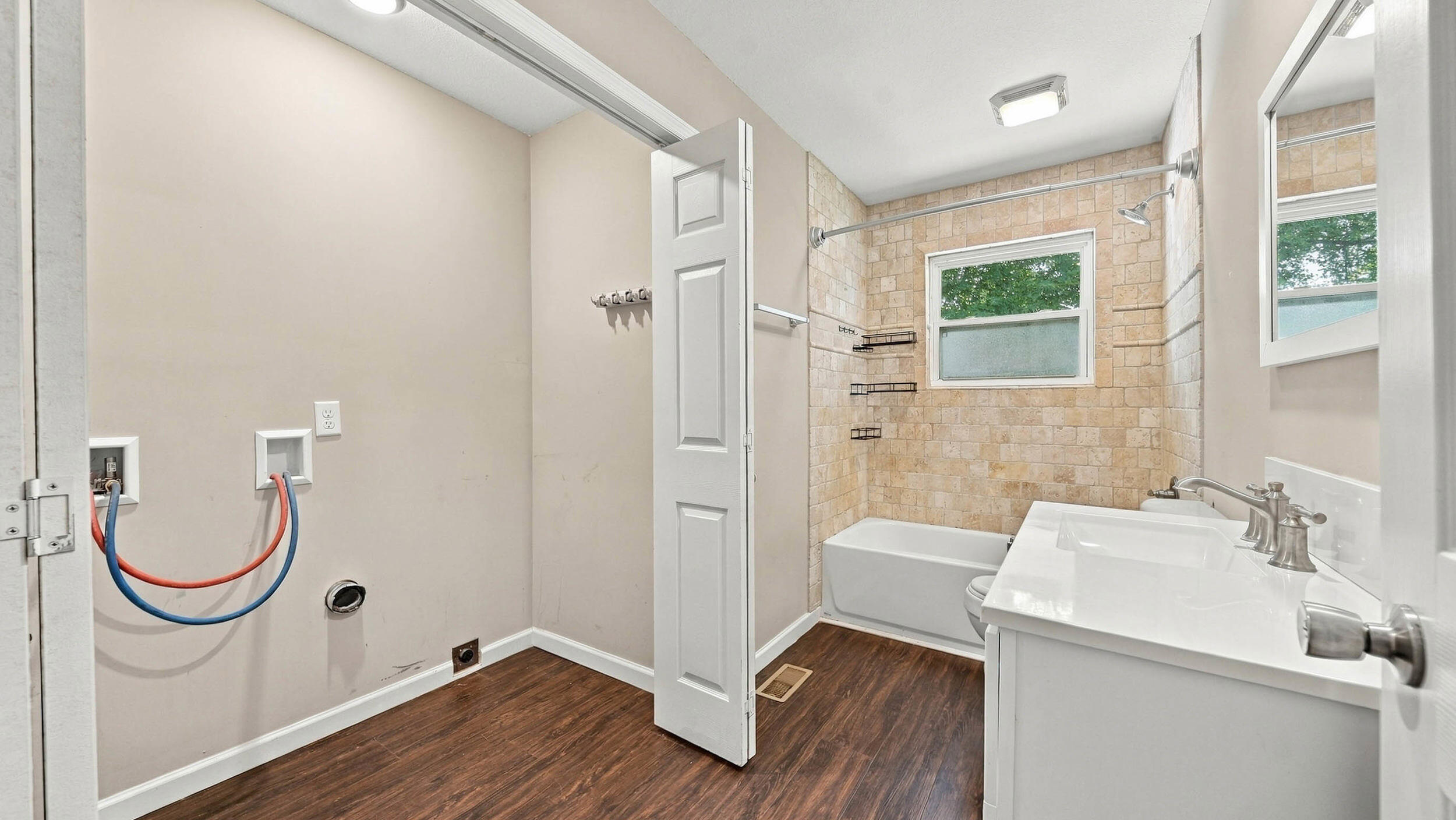 Bathroom with tan tile around the tub, a white vanity, and exposed washer hookups.