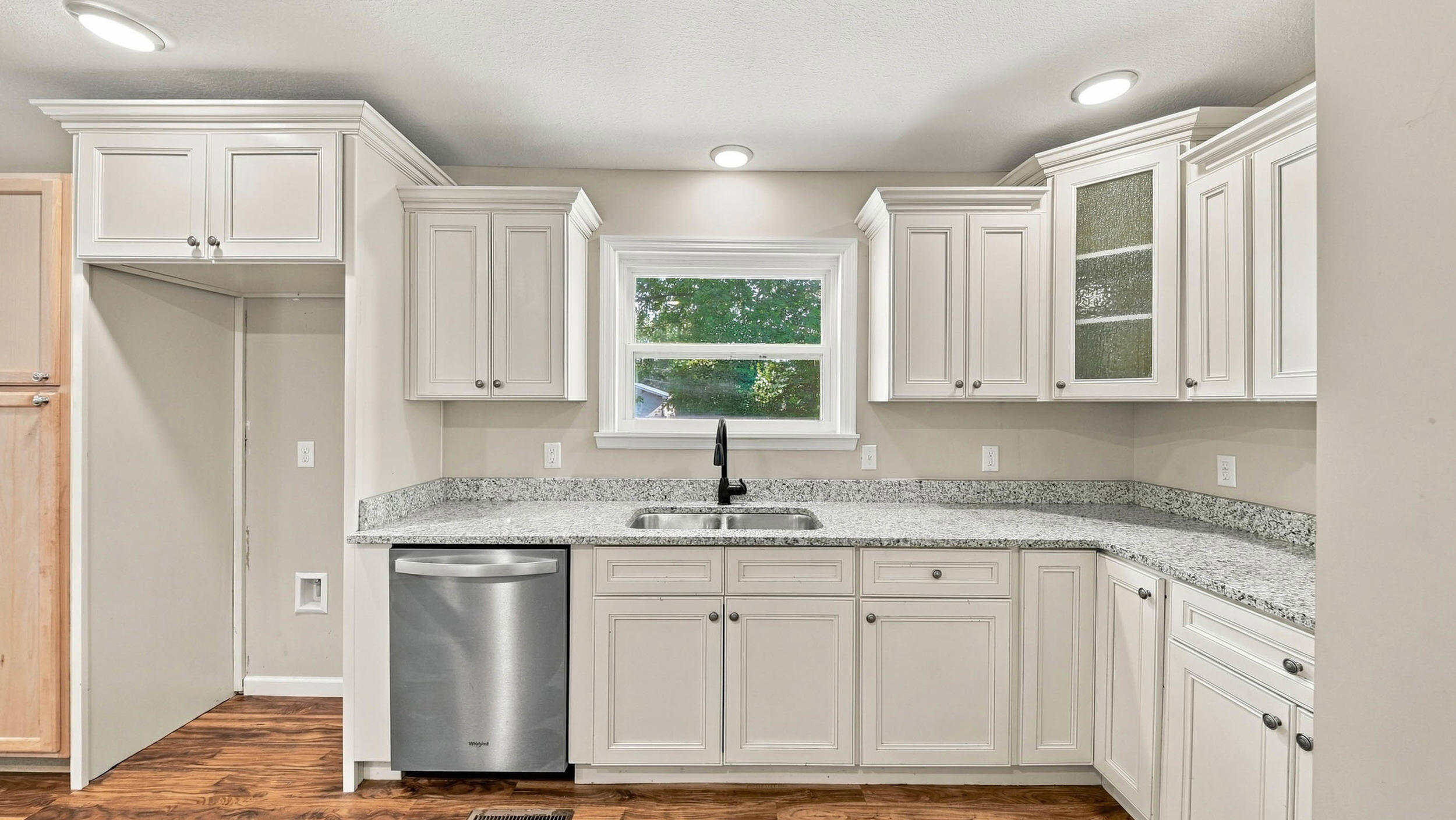 Kitchen with white cabinets, speckled countertops, and a sink beneath a window.