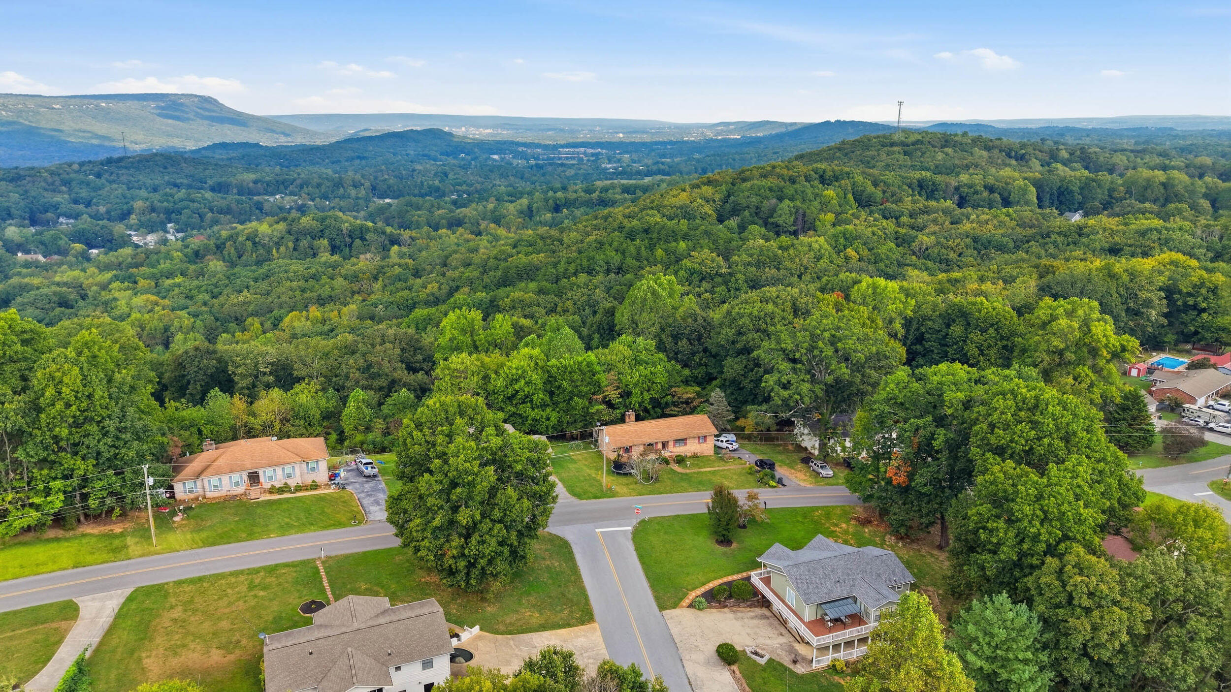 Aerial view of wooded hills, nearby homes, and distant mountain ridges.