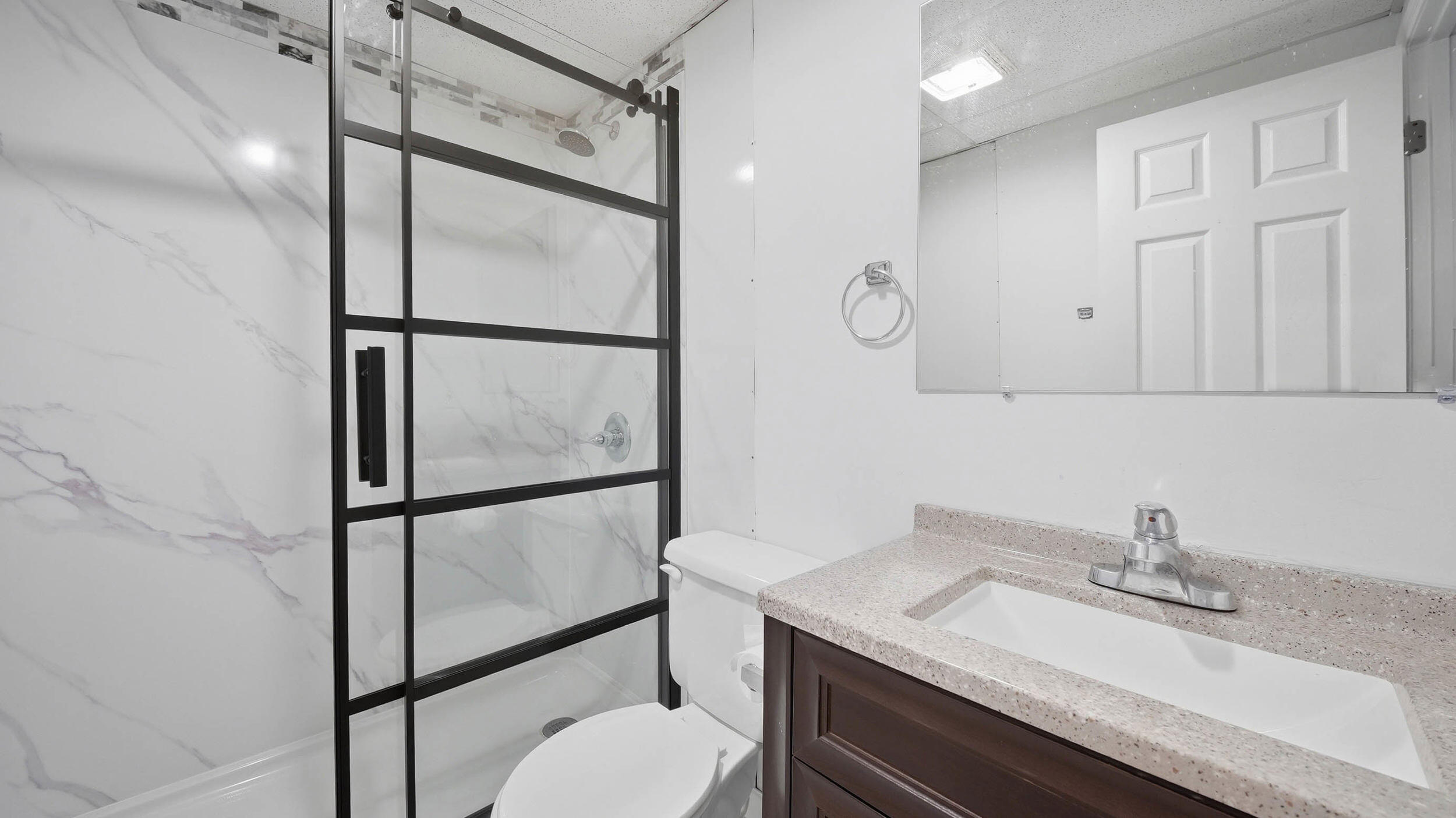 Bathroom with a black-framed glass shower, marble-look walls, and dark wood vanity.