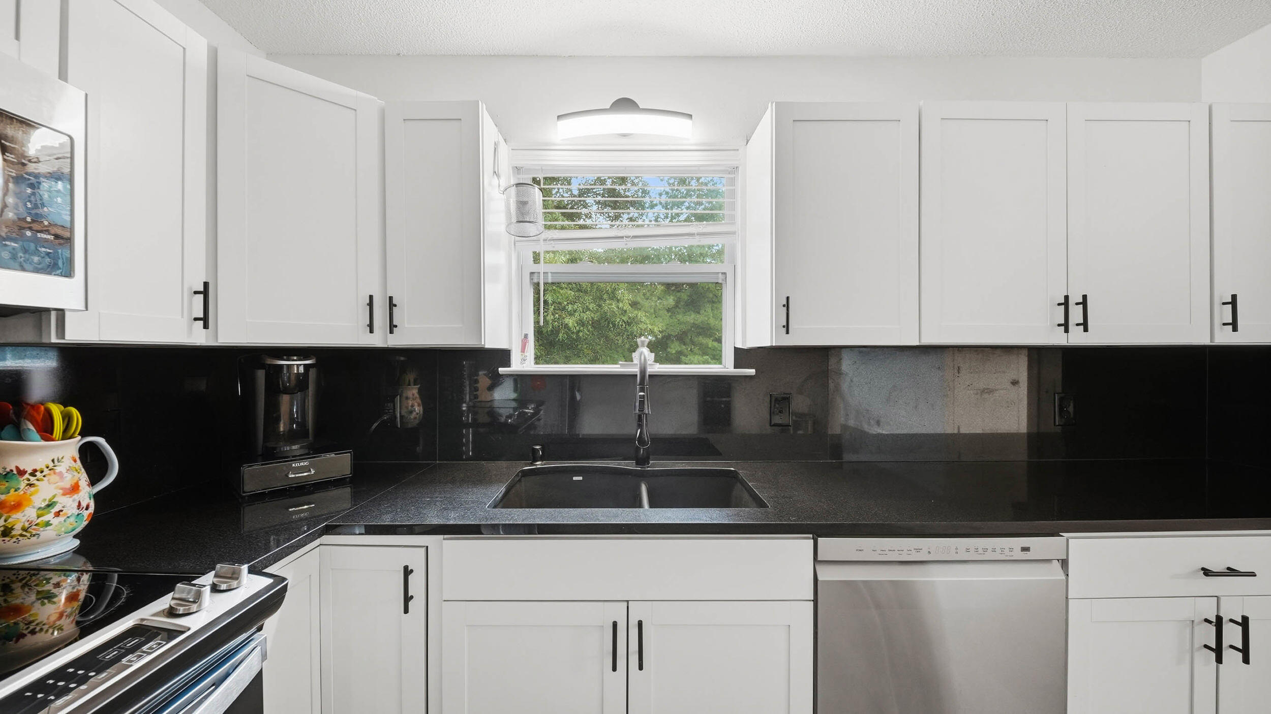 Kitchen with white cabinets, black counters, and a sink beneath a window.
