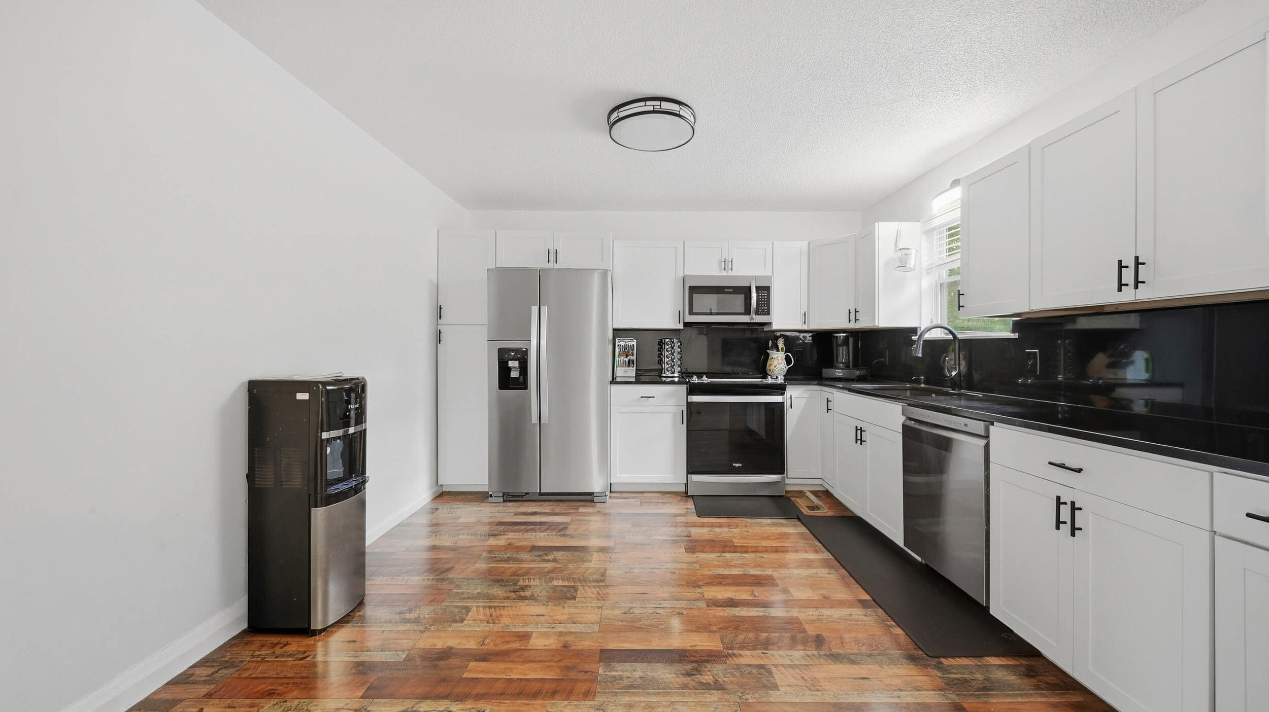 Modern kitchen with white cabinets, black countertops, stainless steel appliances, and multicolored wood-look flooring.