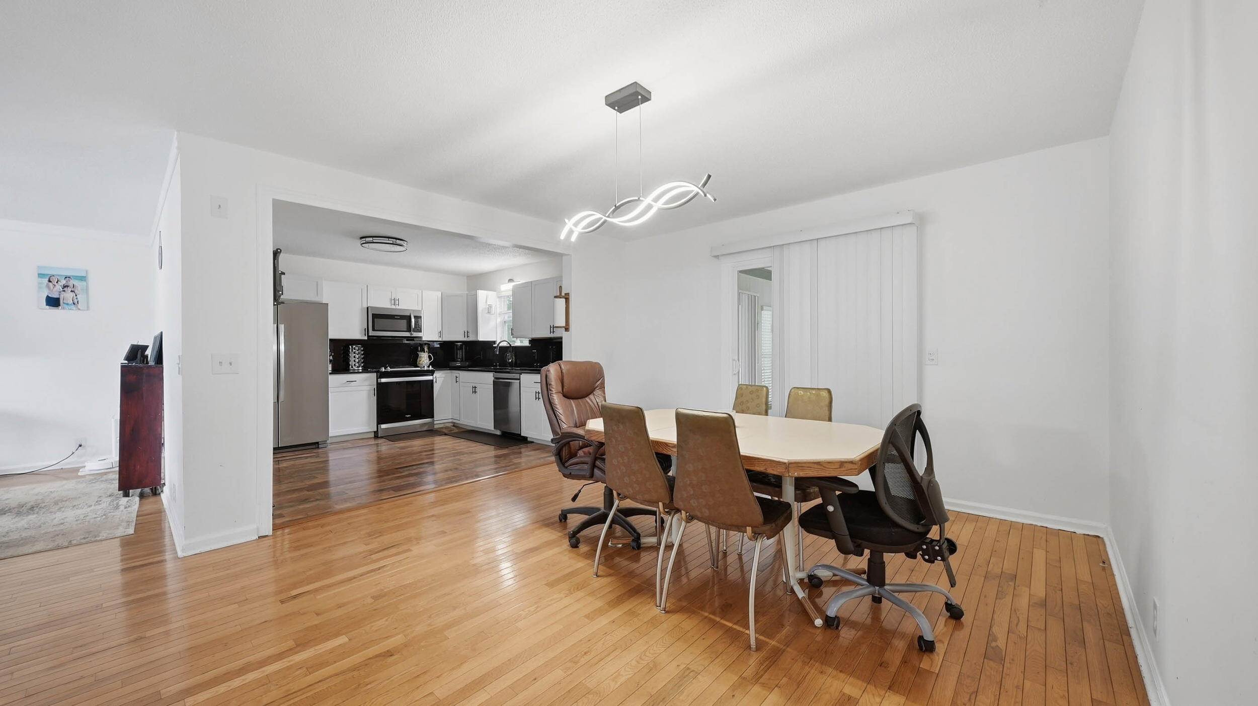 Dining area with hardwood floors and a table opening onto a white kitchen with dark countertops.