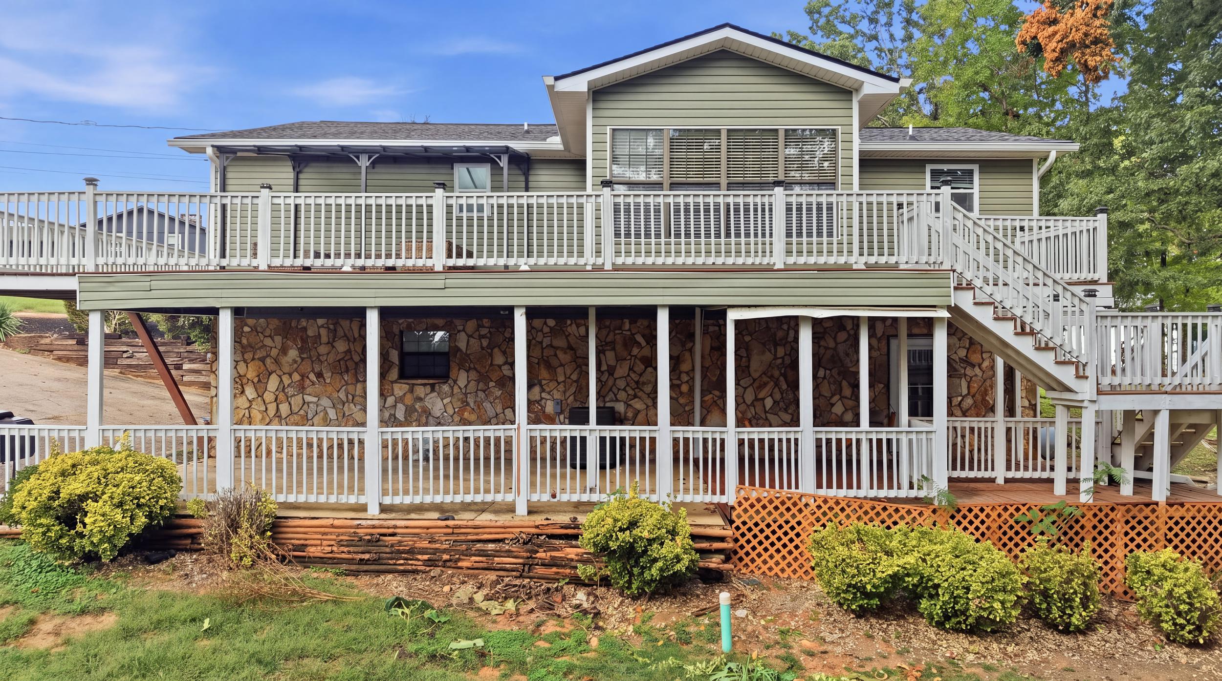 Raised home’s rear exterior with a white-railed deck, exterior stairs, and stone-clad lower level.