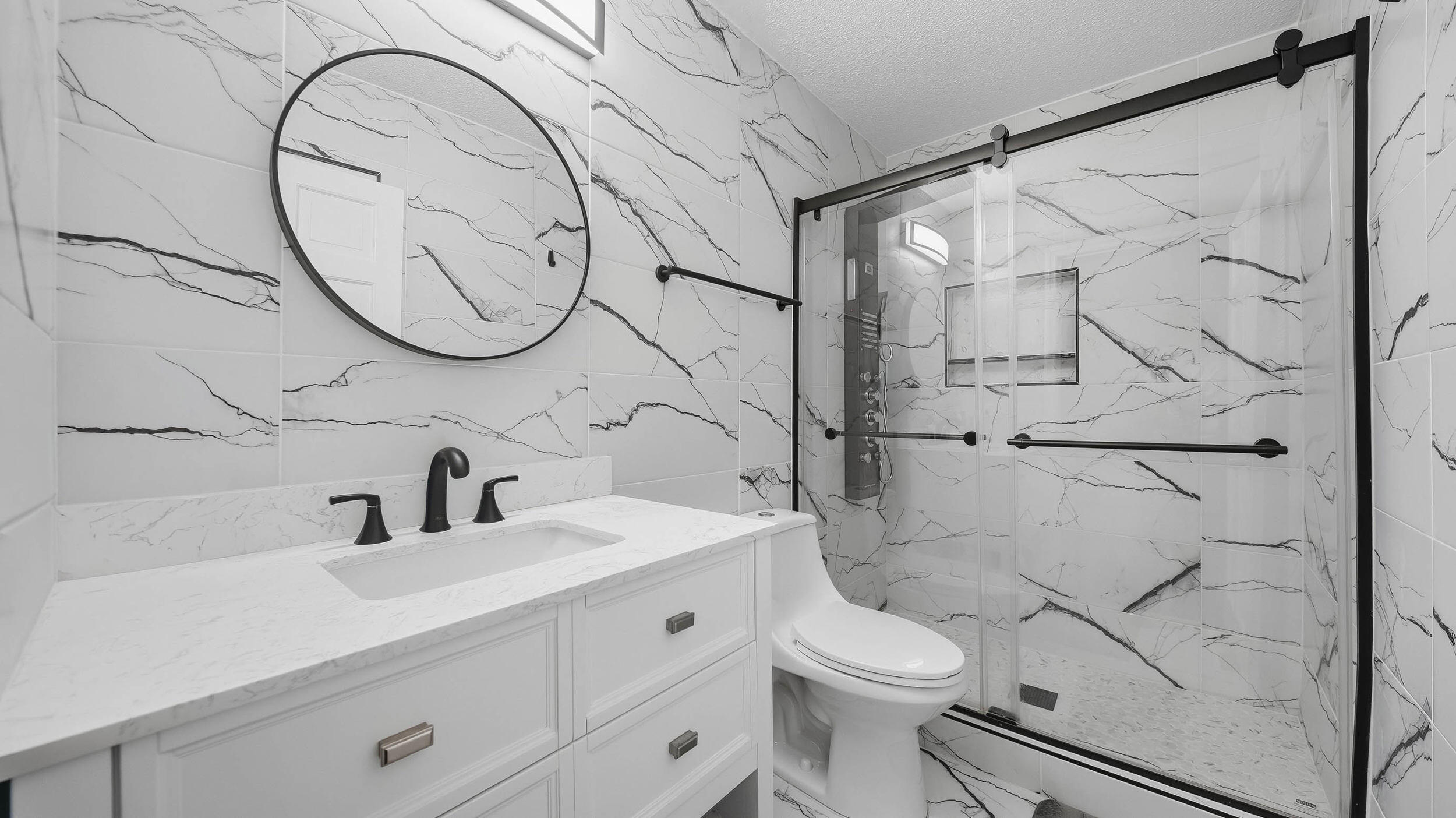 Modern bathroom with marble-look veined tile, a white vanity, round mirror, and glass shower.