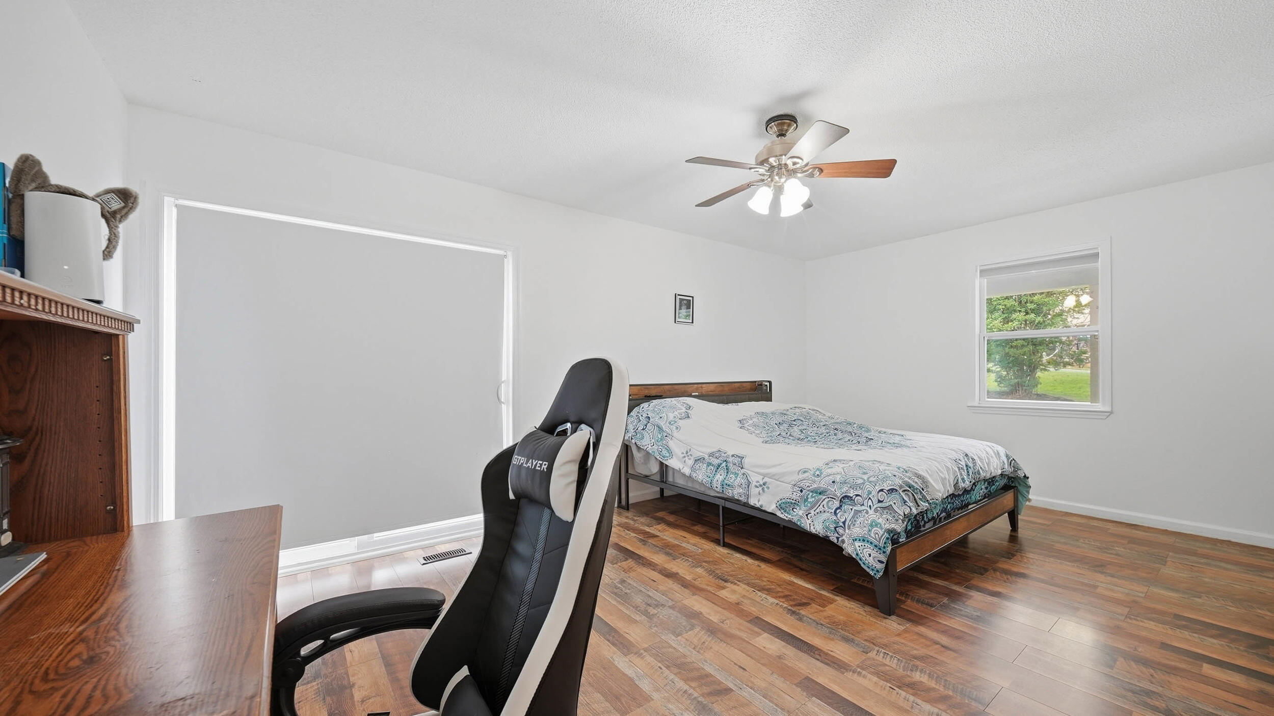 Furnished bedroom with patterned bedding, warm wood floors, and a black-and-white gaming chair.
