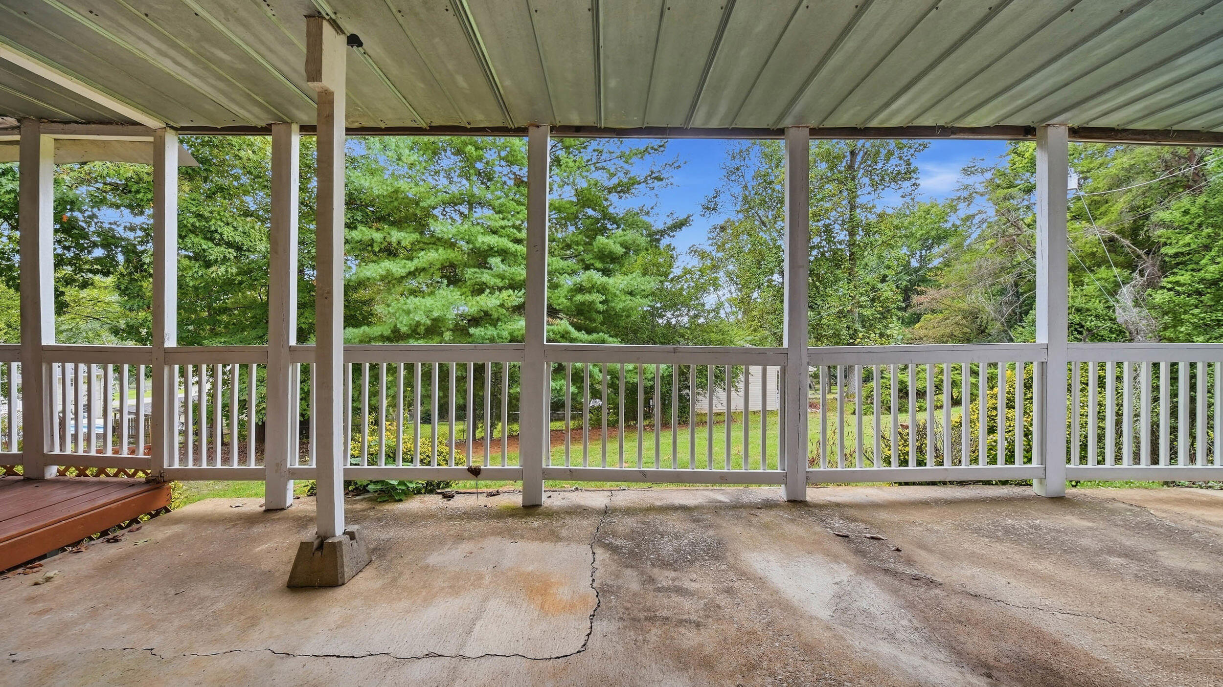 Covered concrete patio with white railings overlooking a leafy backyard.