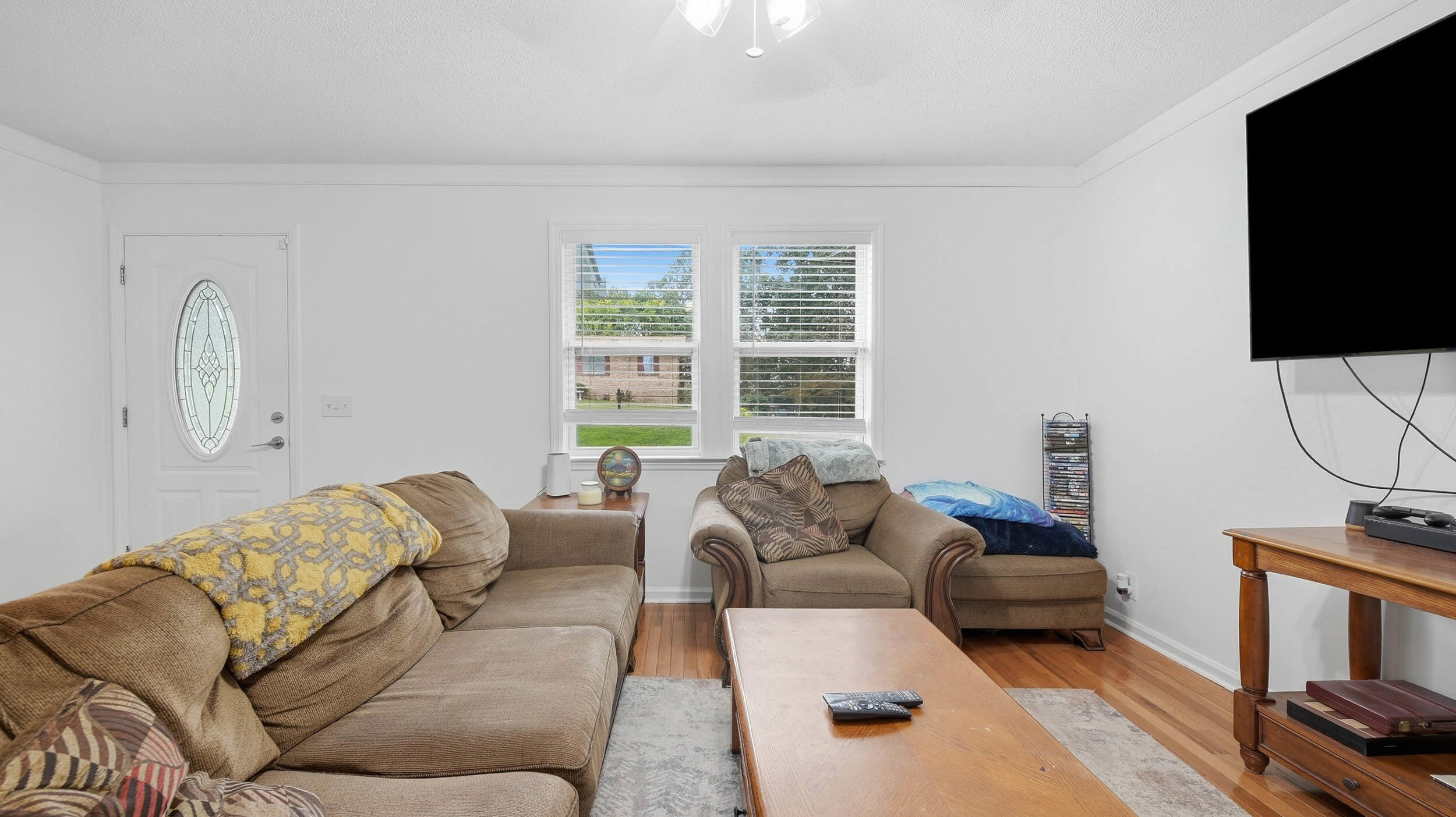 Furnished living room with brown sofas, hardwood floors, and two bright windows.