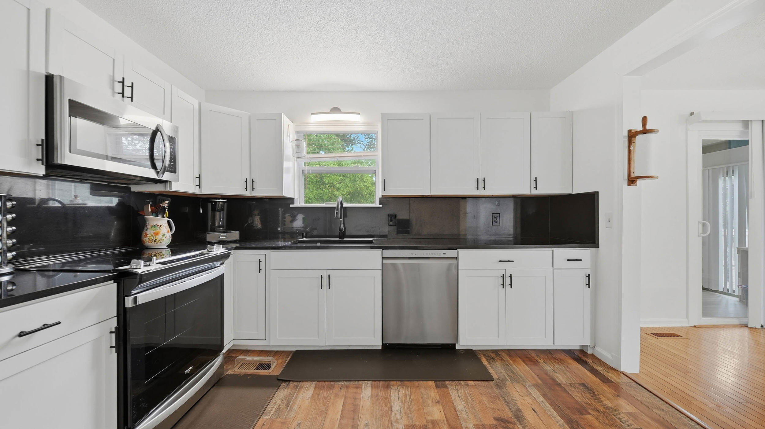 Kitchen with white cabinets, dark counters, stainless appliances, and a sink beneath a window.