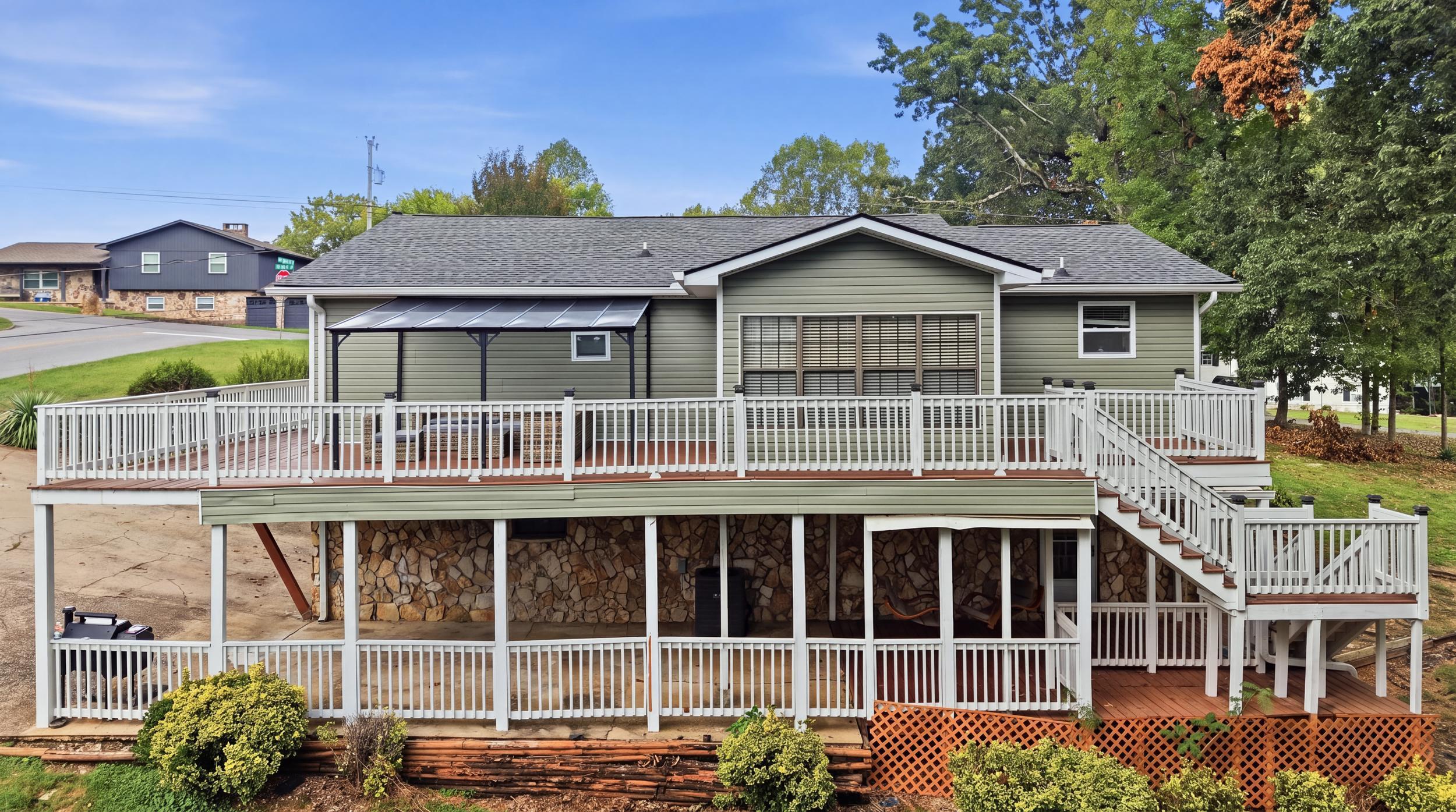 Rear of a gray-green house with a large white-railed deck and covered patio.