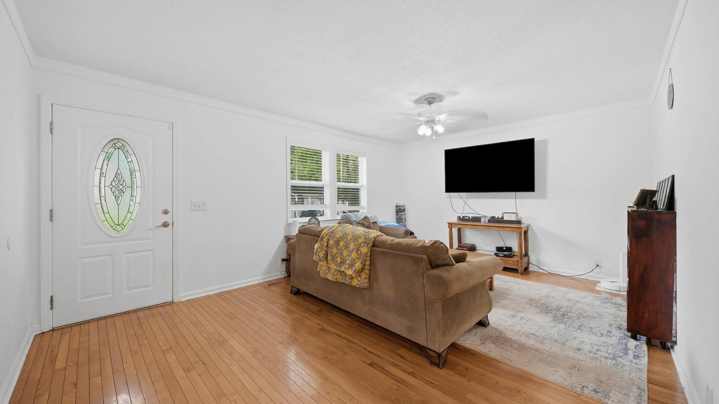 Living room with hardwood floors, brown sofa, and a front door with an oval glass panel.