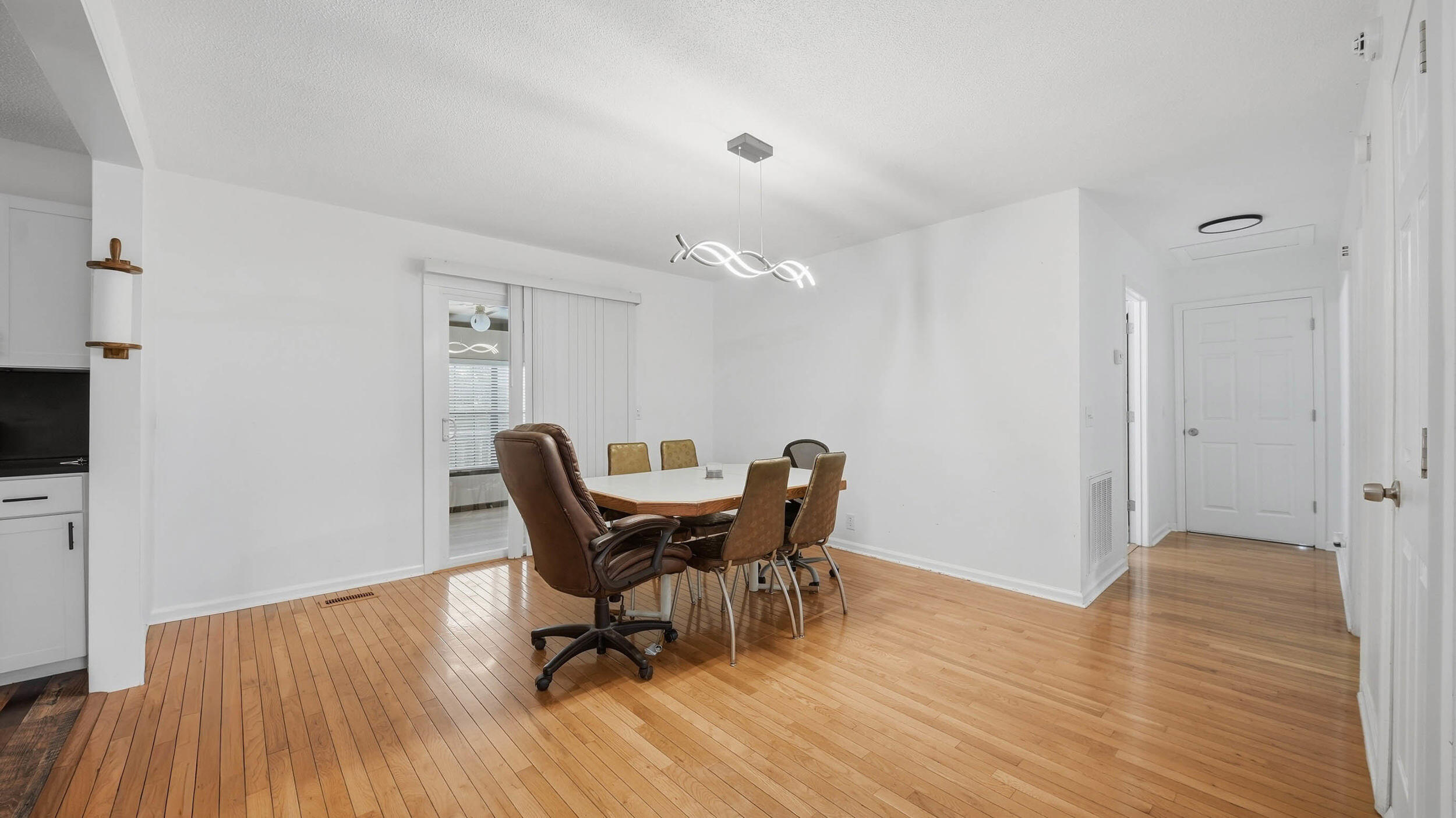 Dining area with a table, chairs, hardwood floors, and a modern pendant light.