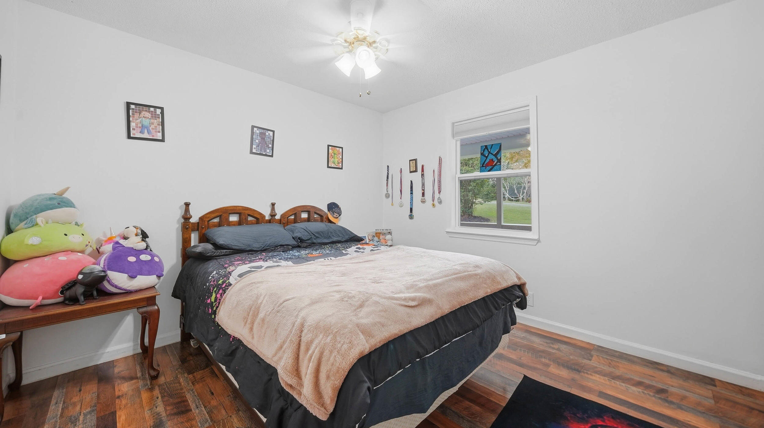 Bedroom with a dark wood bed, plush toys on a side table, and medals displayed beside the window.