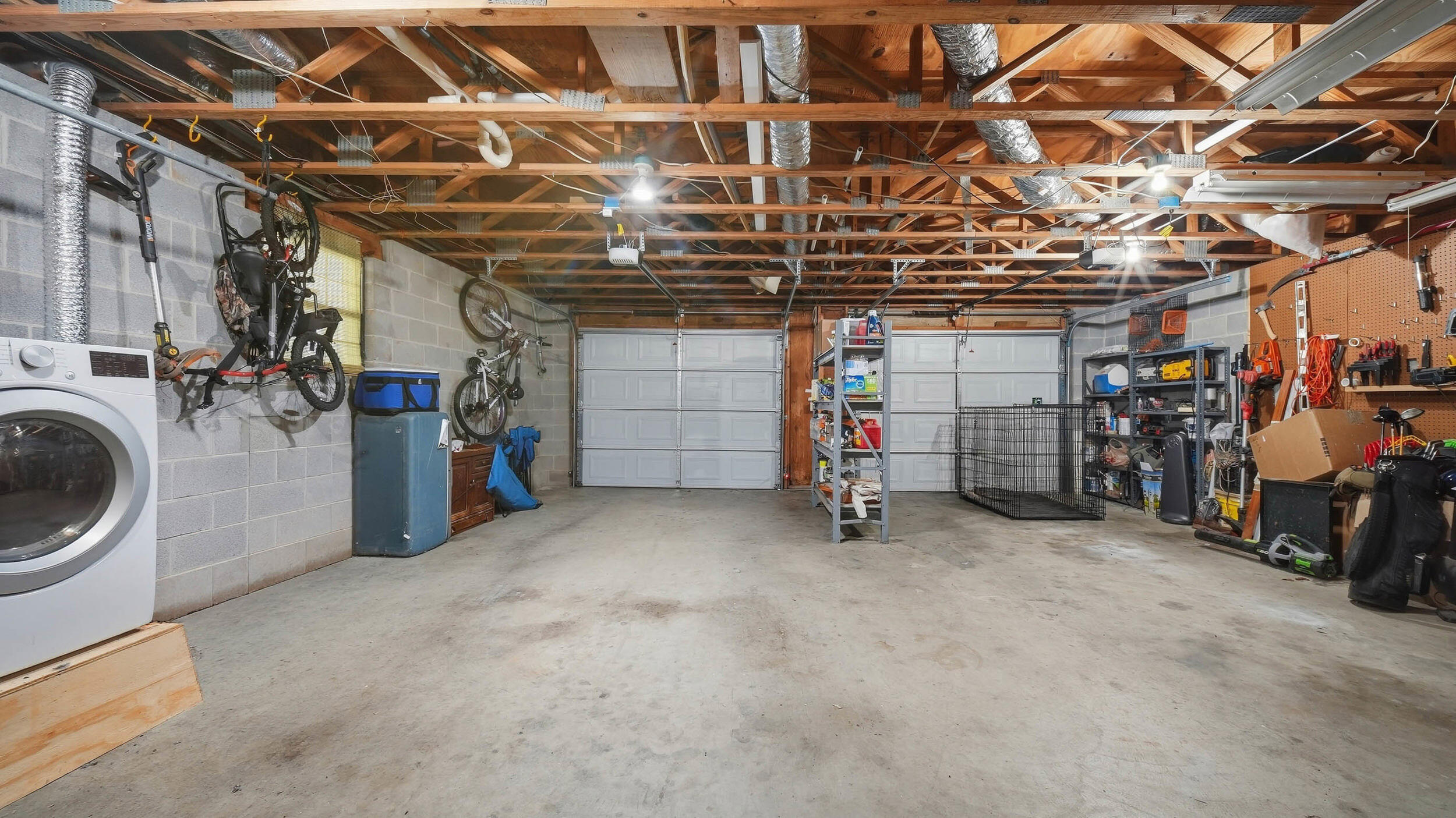 Spacious garage with two white doors, exposed ceiling joists, bicycles, storage shelves, and a washing machine.
