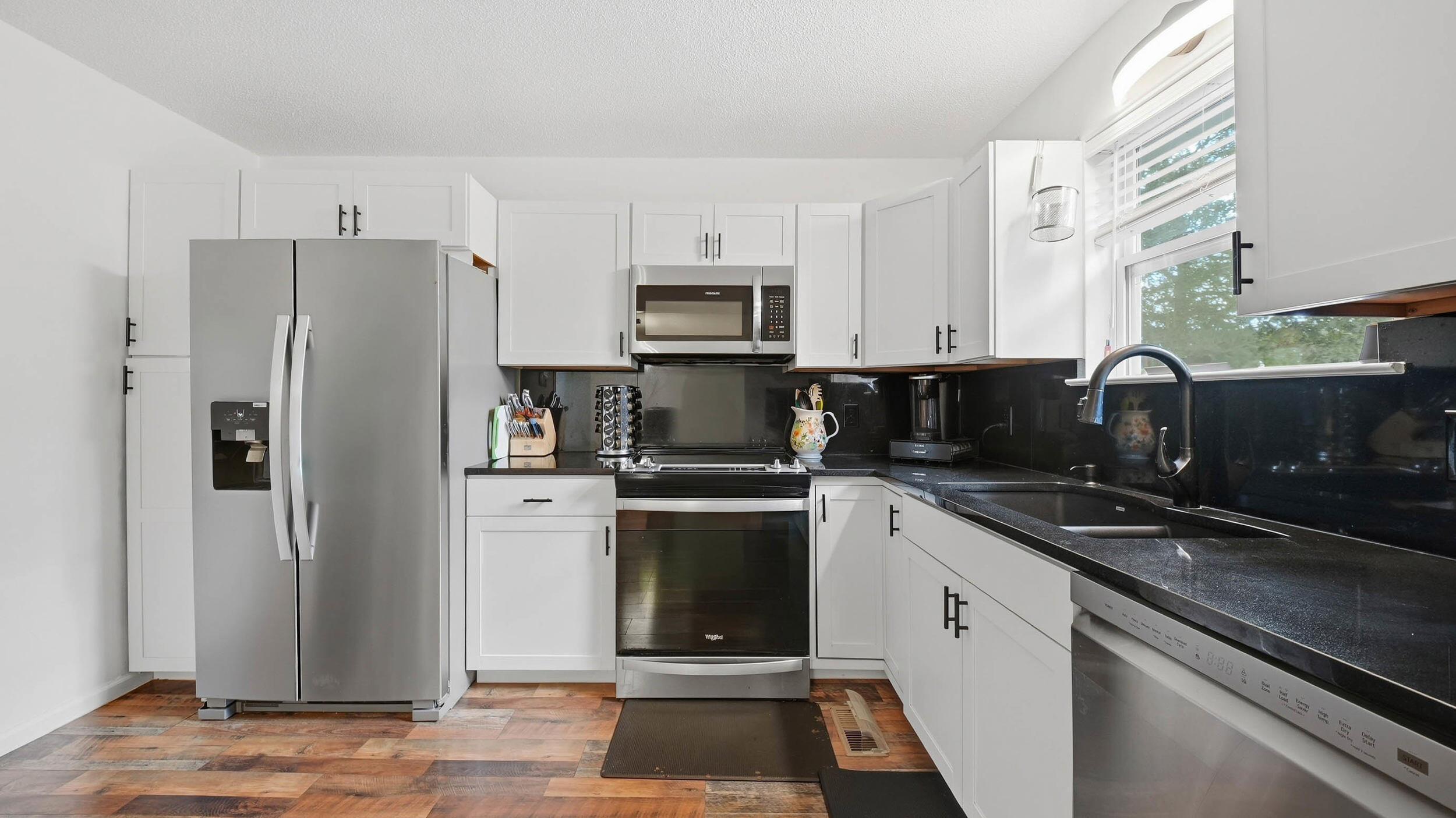 Bright kitchen with white cabinets, dark counters, stainless appliances, and multicolored tile flooring.