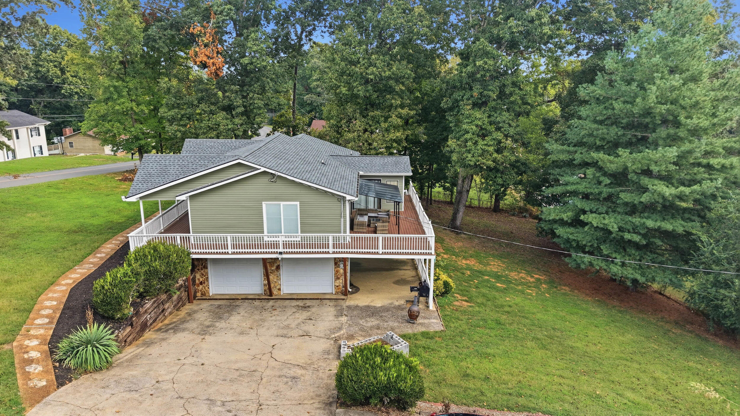 Gray-green house with a broad white-railed deck above two garage doors, surrounded by lawn and trees.