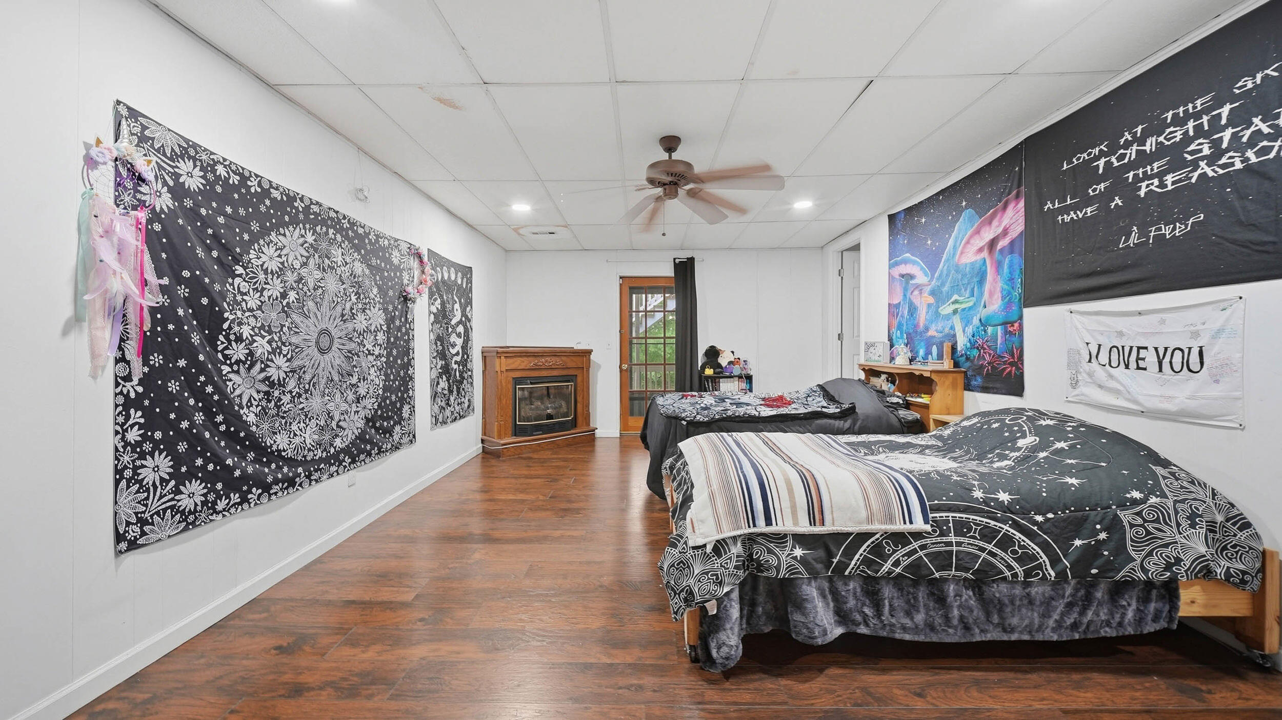 Bedroom with two celestial-patterned beds, wall tapestries, a mushroom mural, and a fireplace.