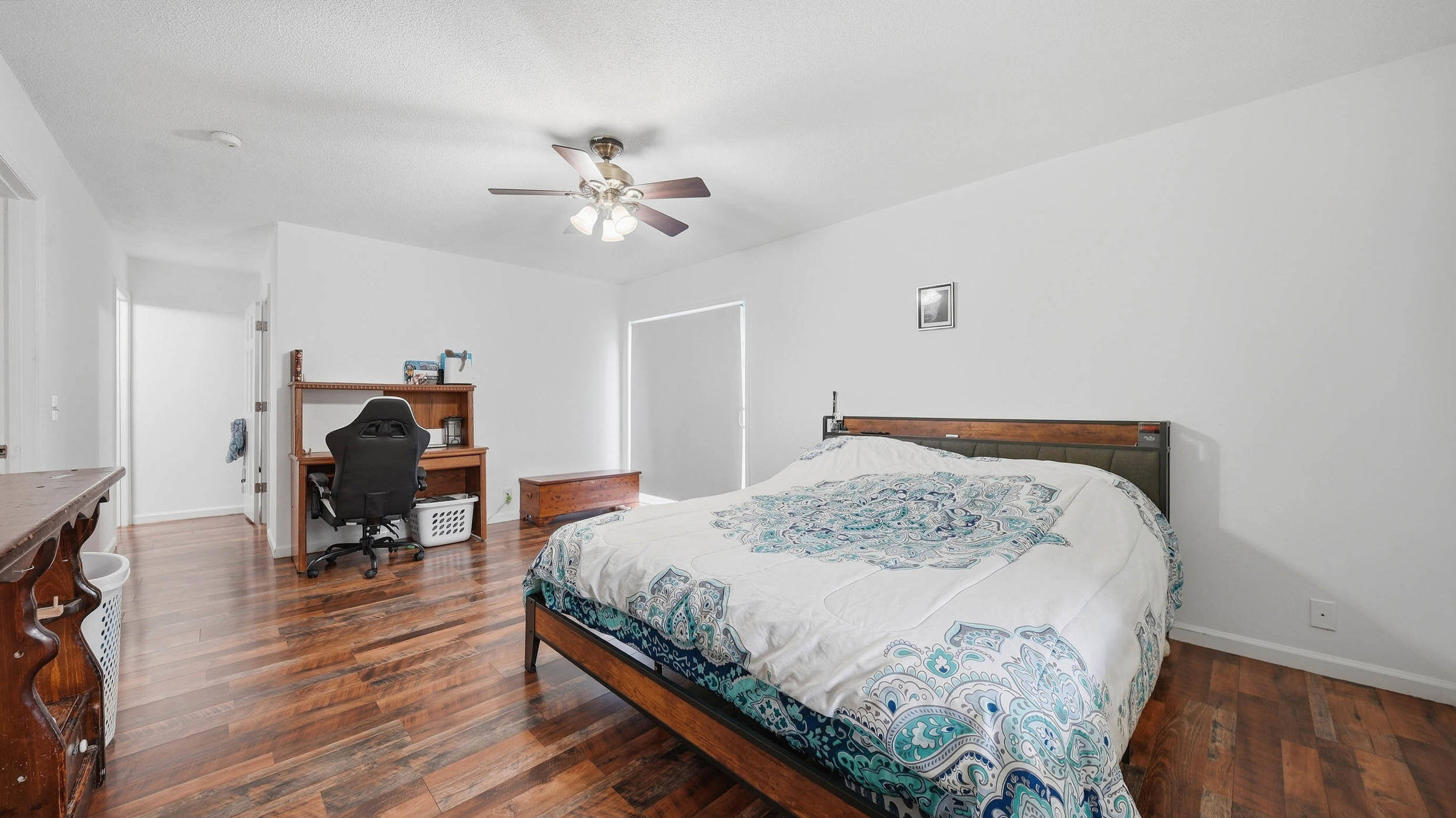 Bedroom with a patterned teal-and-blue comforter, wood floors, and a desk area.