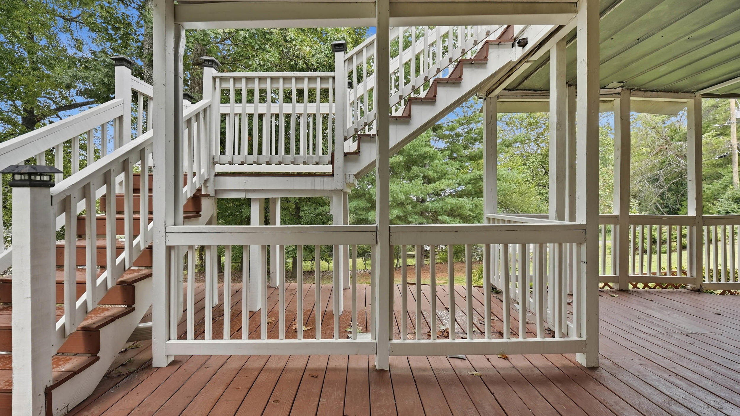 Wooden deck with white railings and multiple stairways, surrounded by trees.