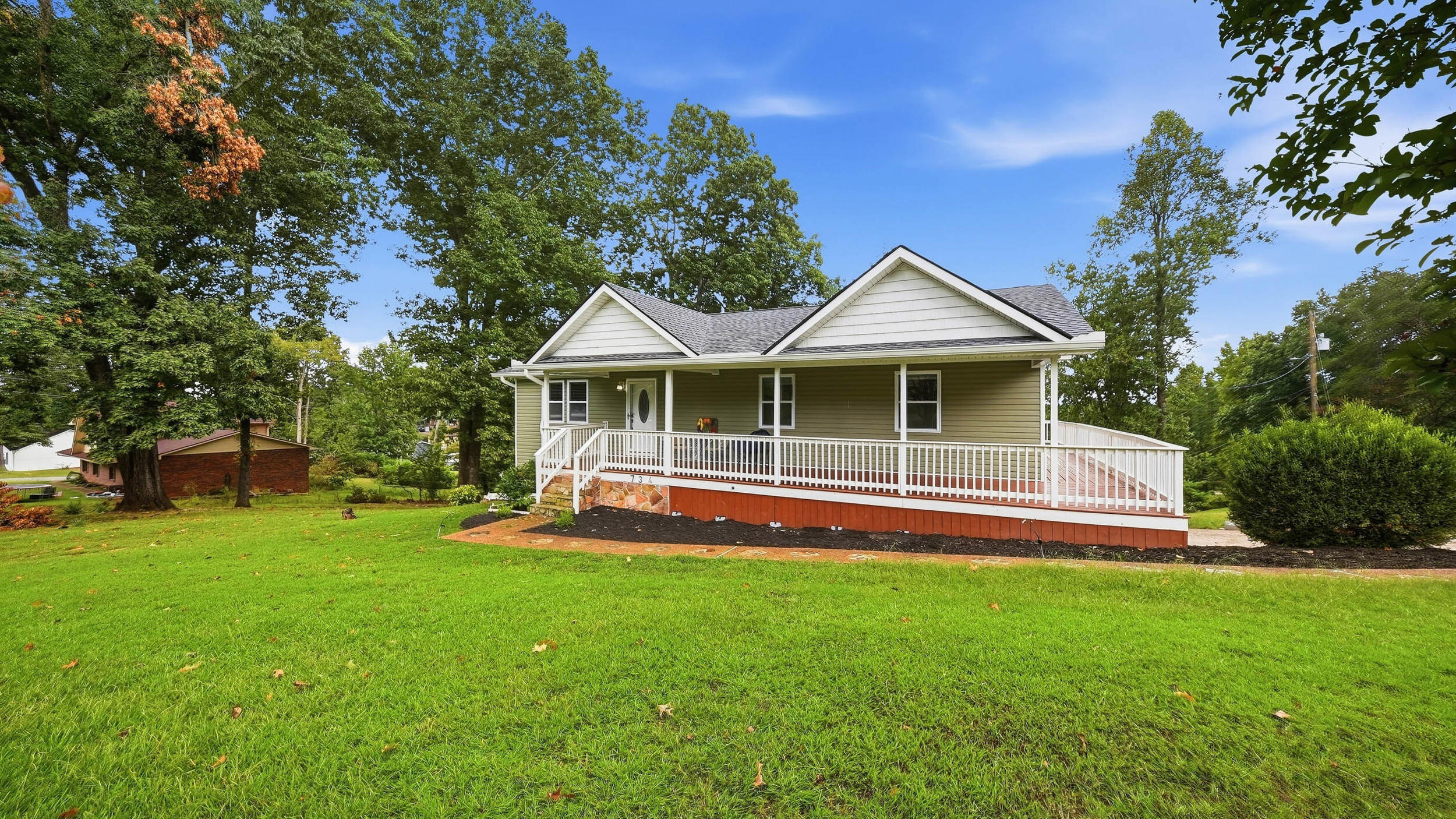 Olive-sided home with a wide white-railed porch, gray gabled roof, and spacious lawn.