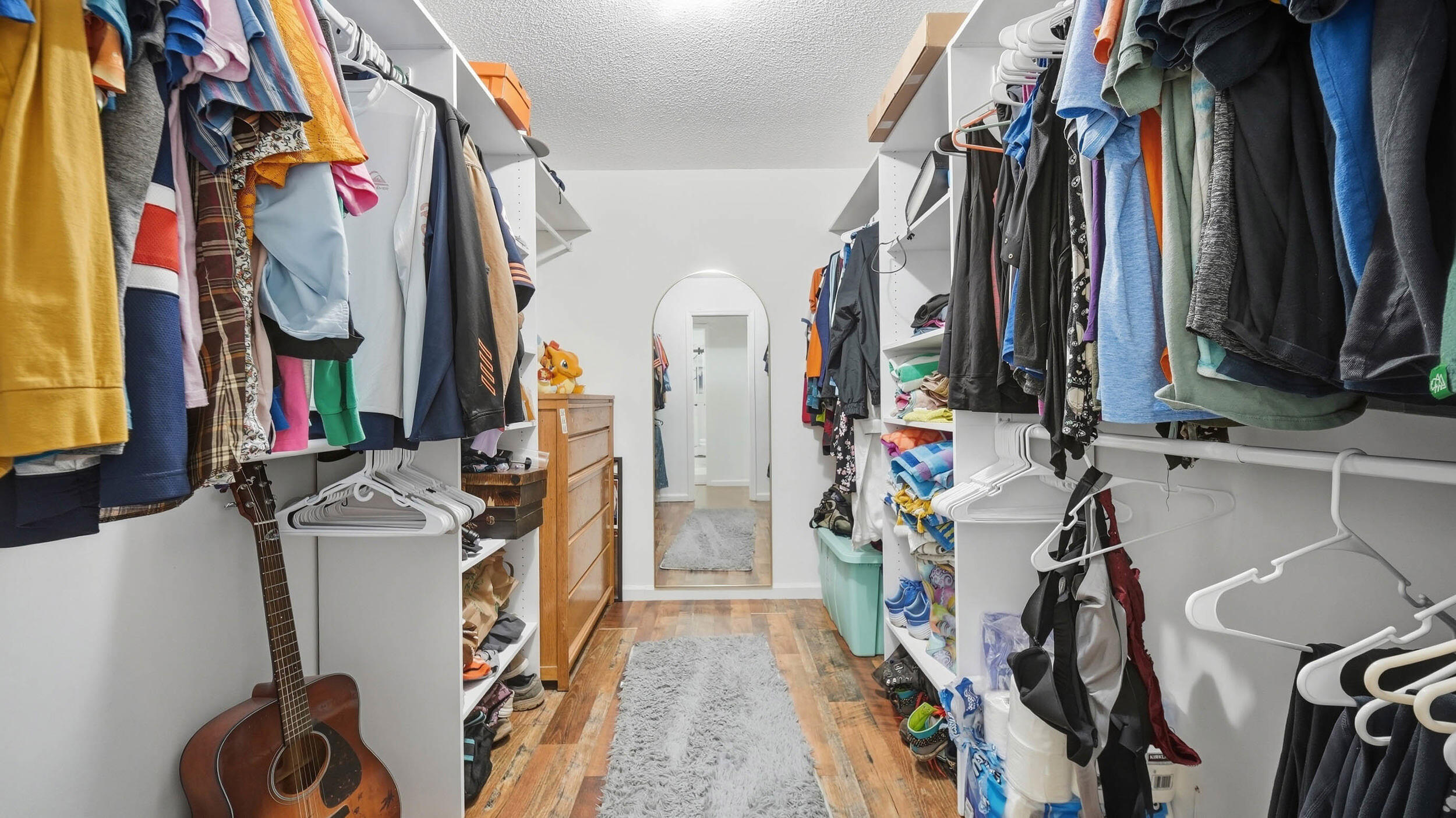 Walk-in closet with extensive shelving, hanging clothes, a full-length mirror, and a guitar.