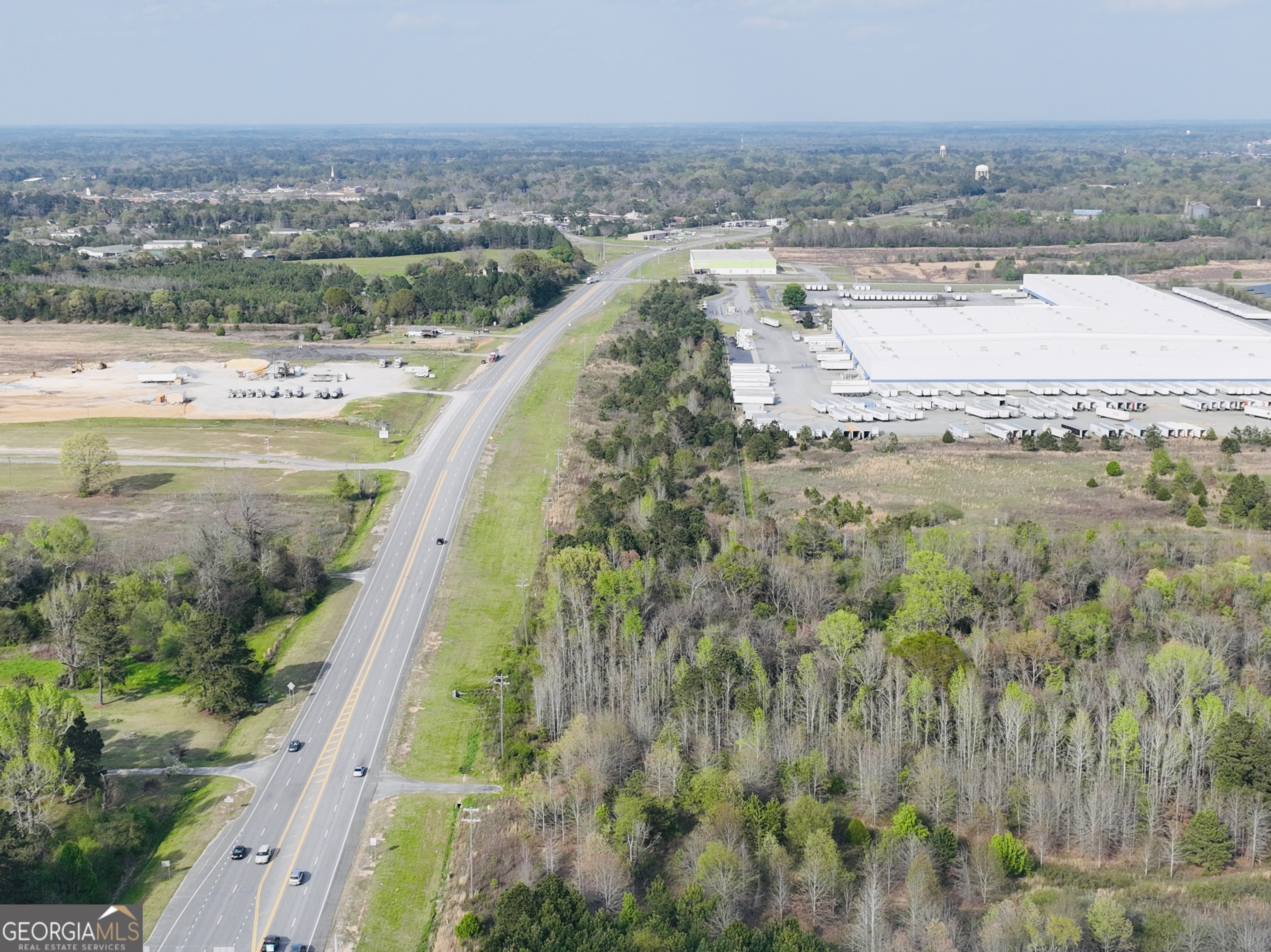 Aerial view of wooded land along a highway beside a large distribution warehouse.