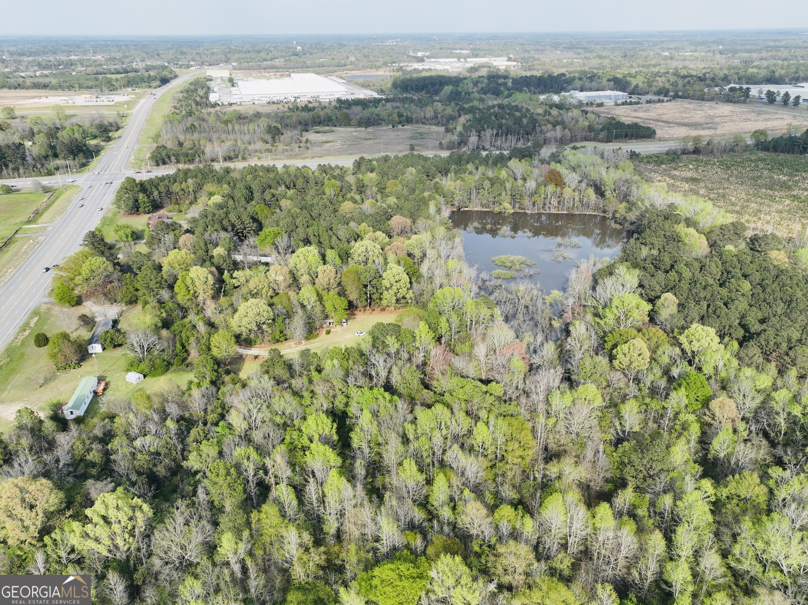 Aerial view of wooded property with a pond beside a major road.