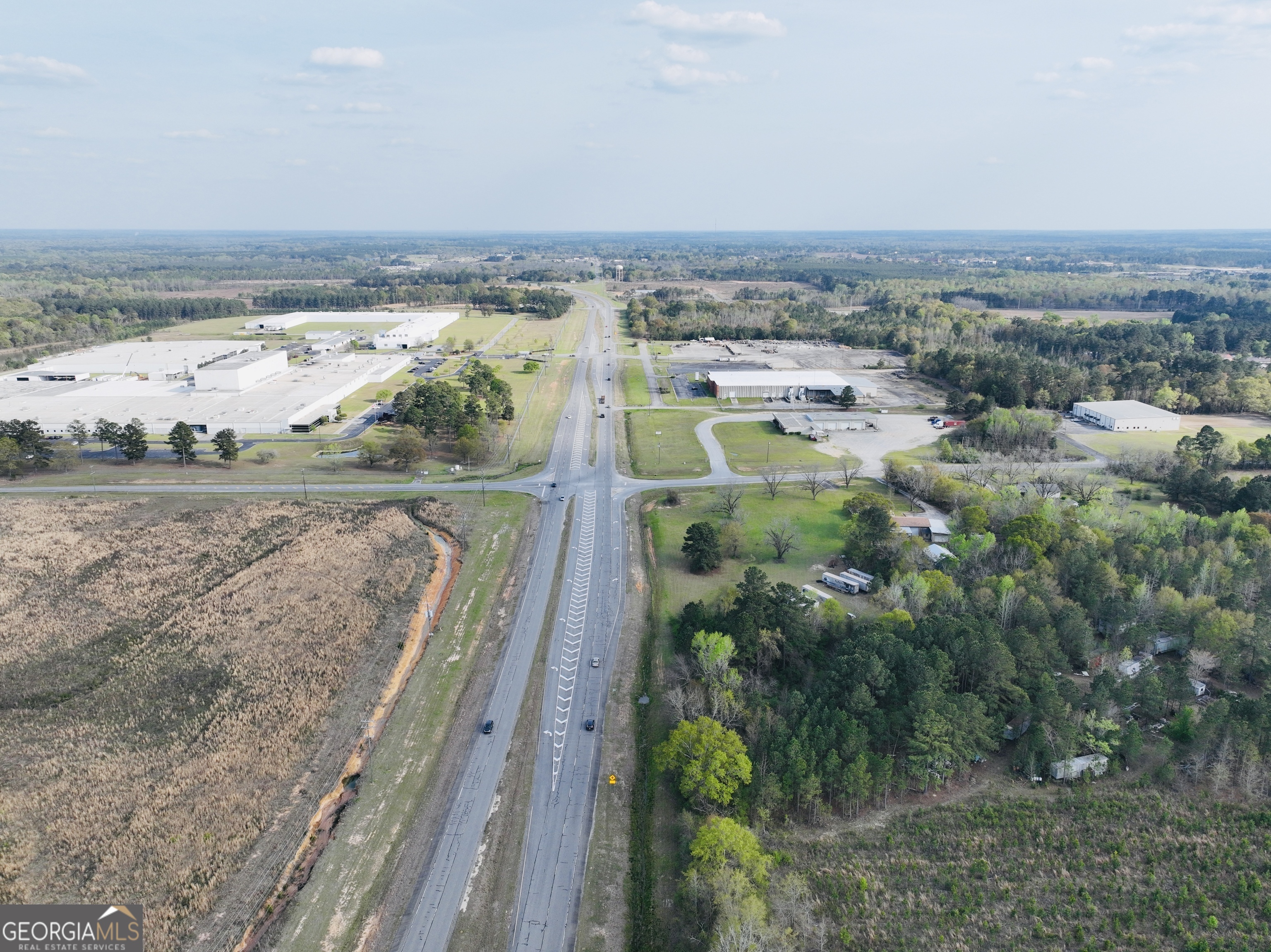 Aerial view of a divided highway bordered by industrial buildings, fields, and wooded land.